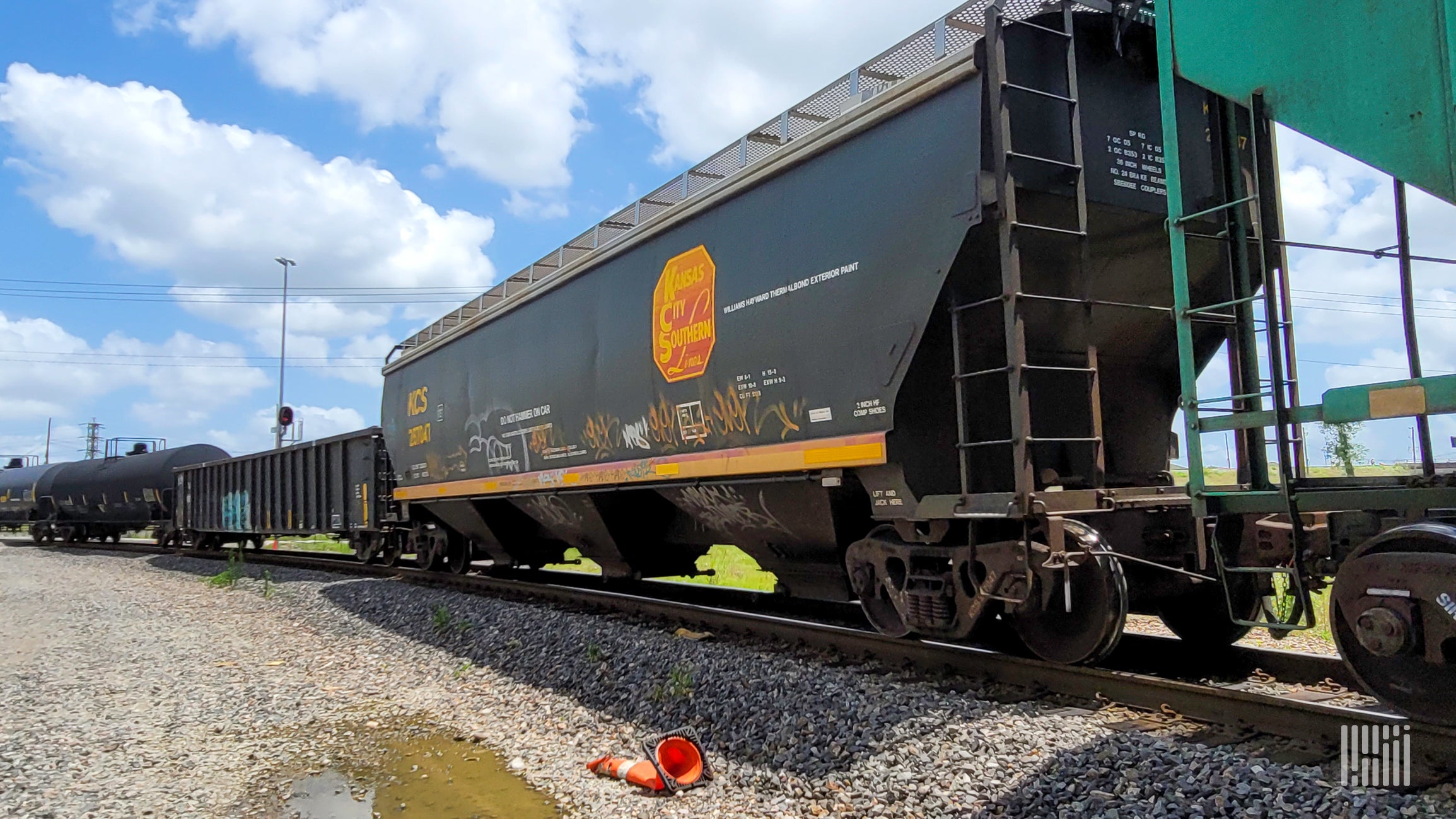 A photograph of a Kansas City Southern grain hopper on a rail track.