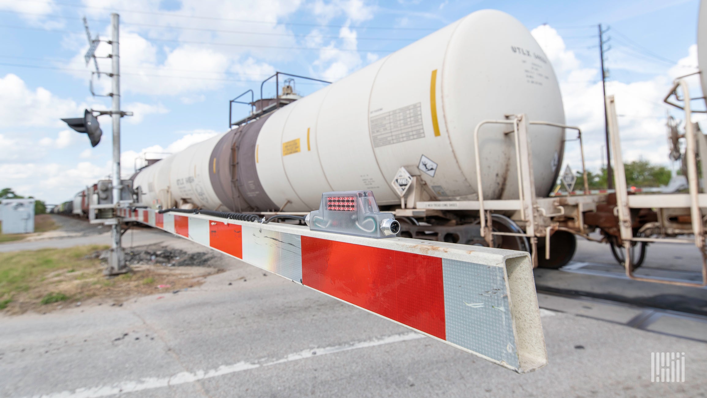 A photograph of a train with tank cars crossing a rail crossing.