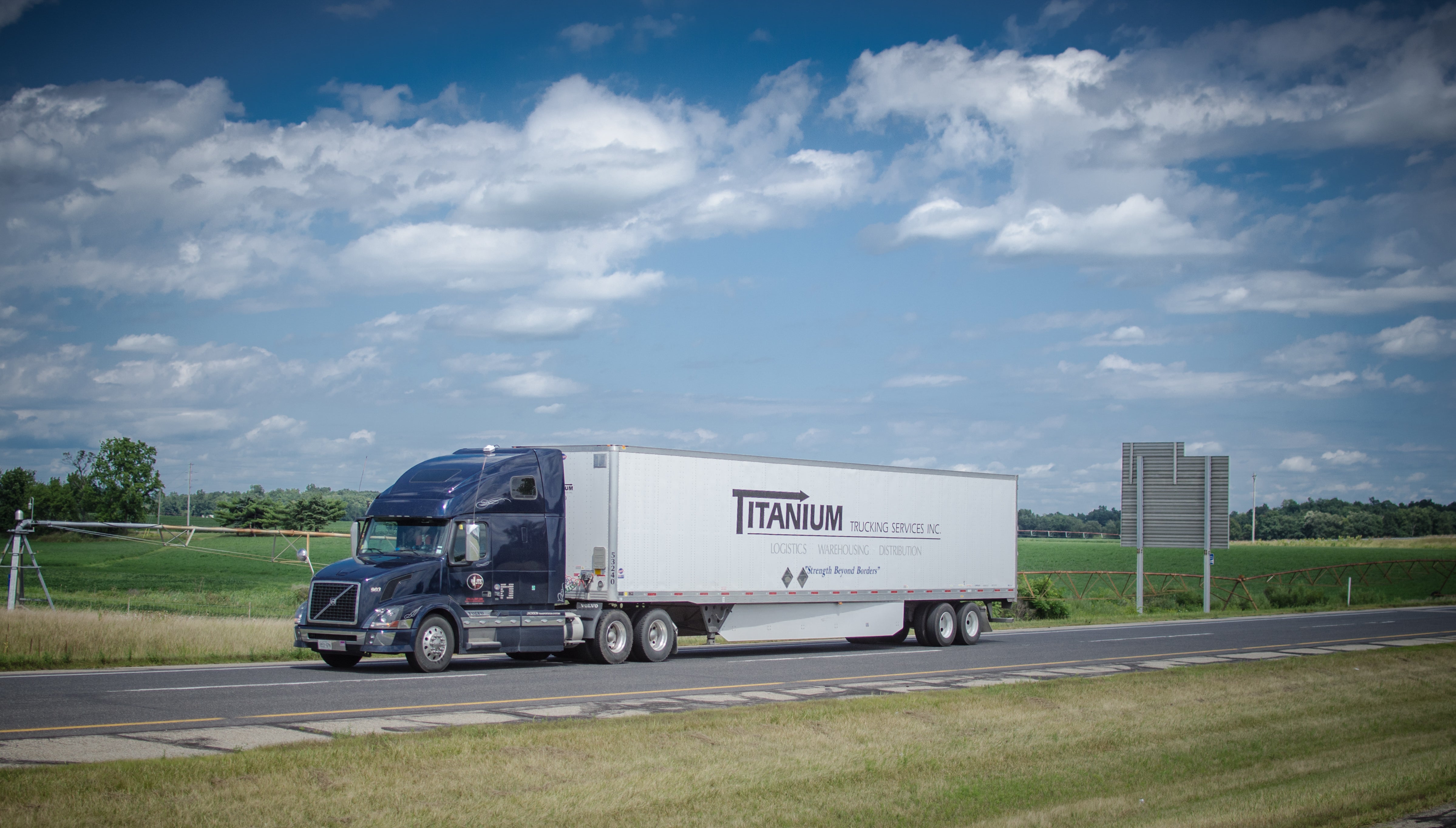 A tractor-trailer from trucking firm Titanium seen from the side on a highway.