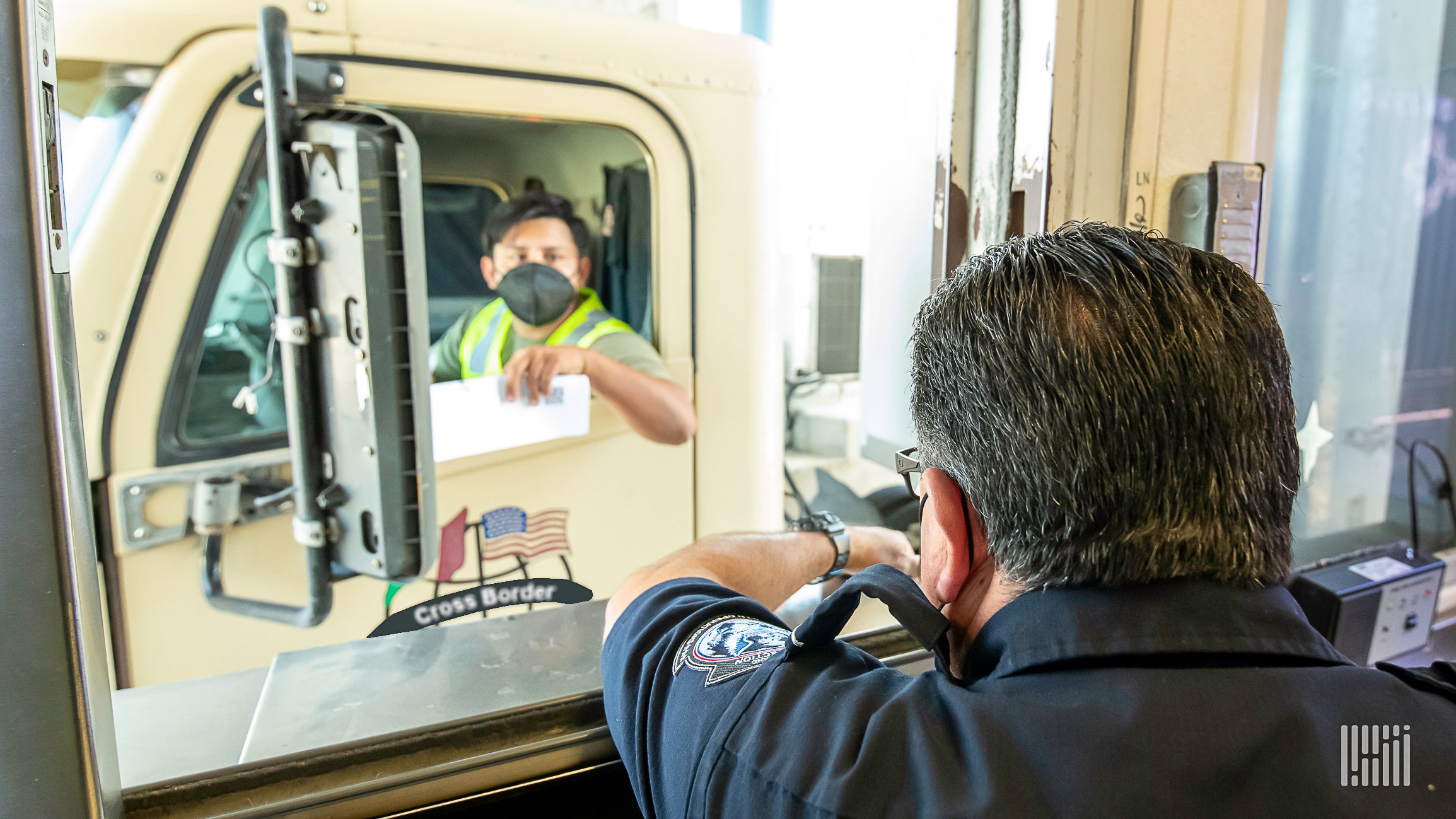 A trucker at the US-Mexico border seen through the window of a US Customs and Border Protection officer illustrate an article about a coming vaccine requriement.