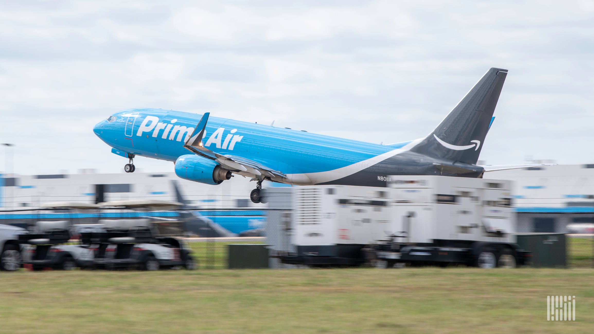 A light blue Amazon Air plane takes off, view from side rear.