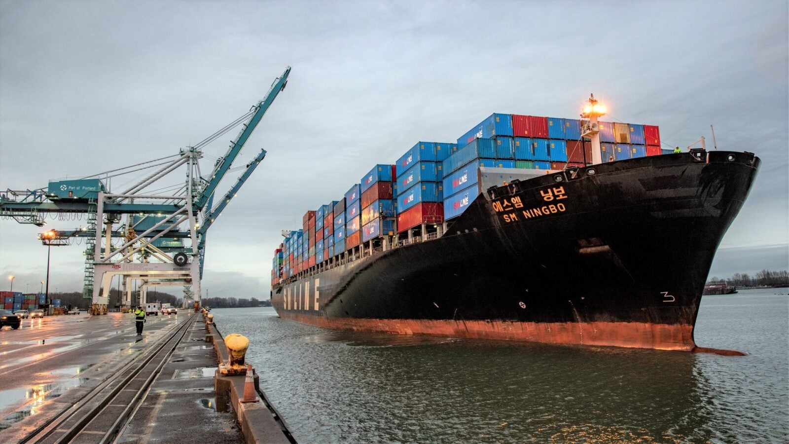 A container vessel pulls next to the dock with cranes in raised position.