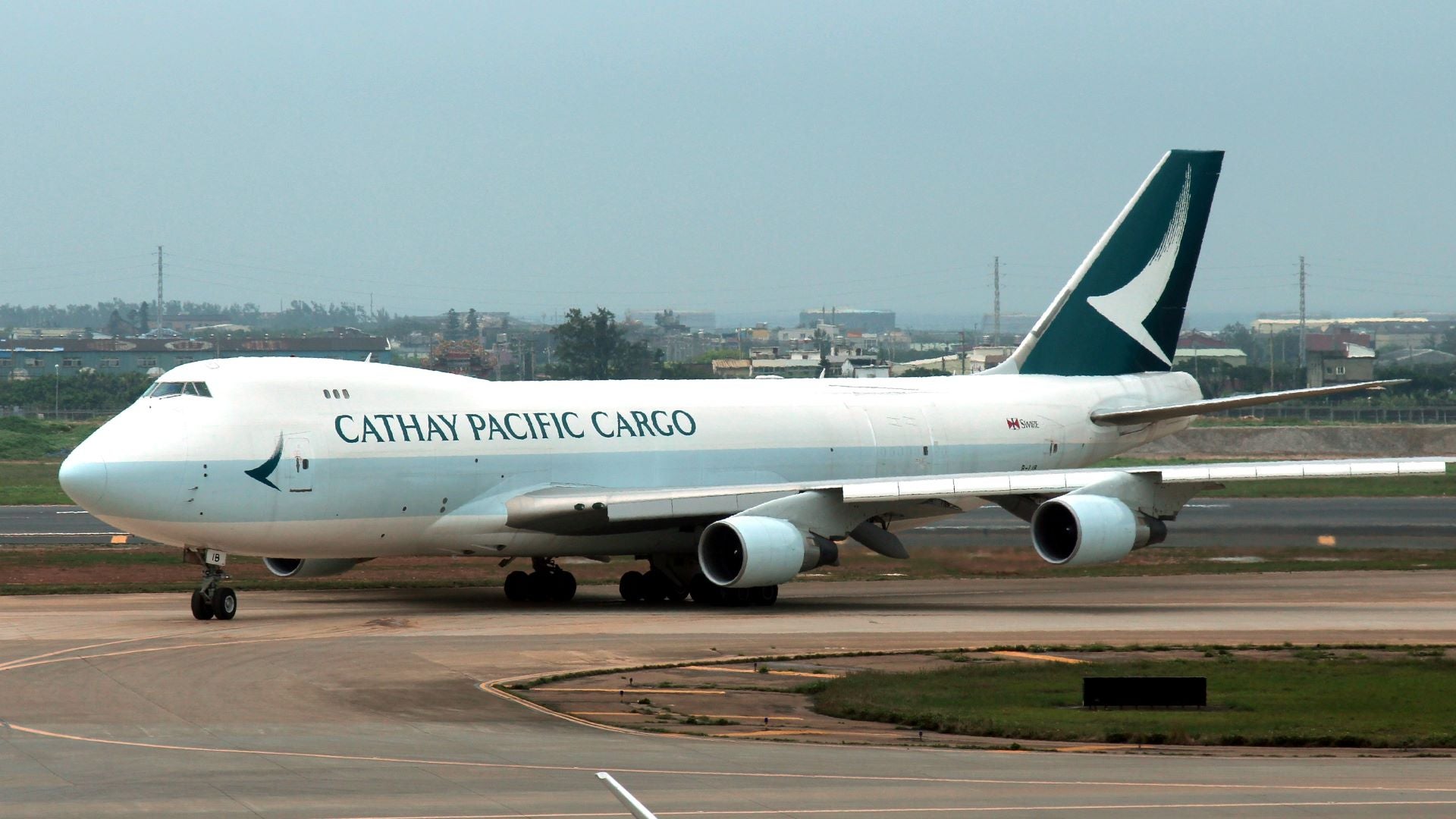 A white Cathay Pacific 747 jumbo jet with green tail turns on the runway.