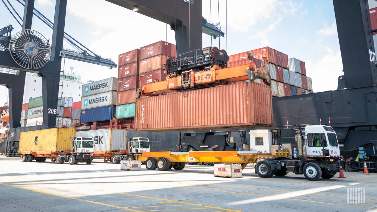 A crane lowers a container from a vessel onto a shuttle cart.