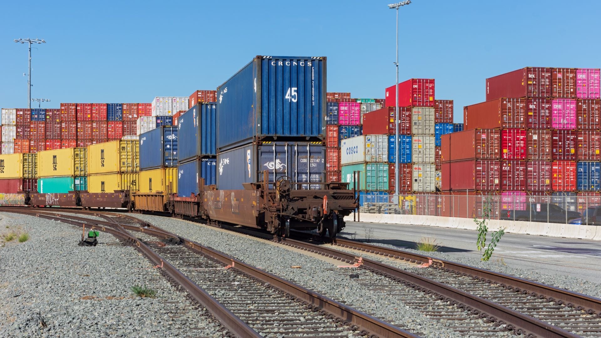 Multicolor containers stacked on ground and on a freight train.