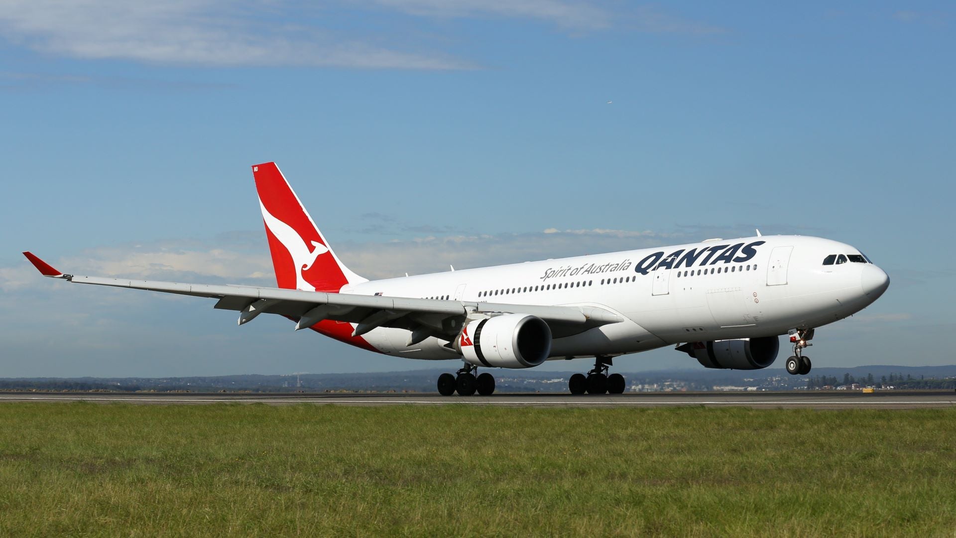 A Qantas jetliner with white body and red tail on the ground.