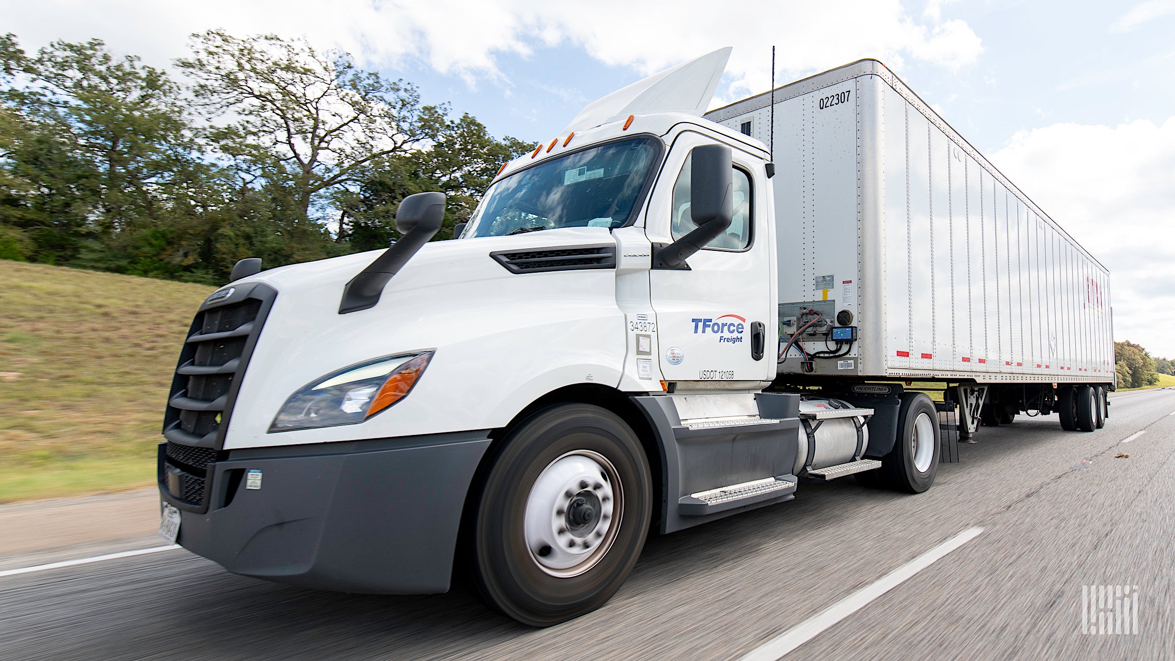 A white TForce Freight truck travels on a highway.