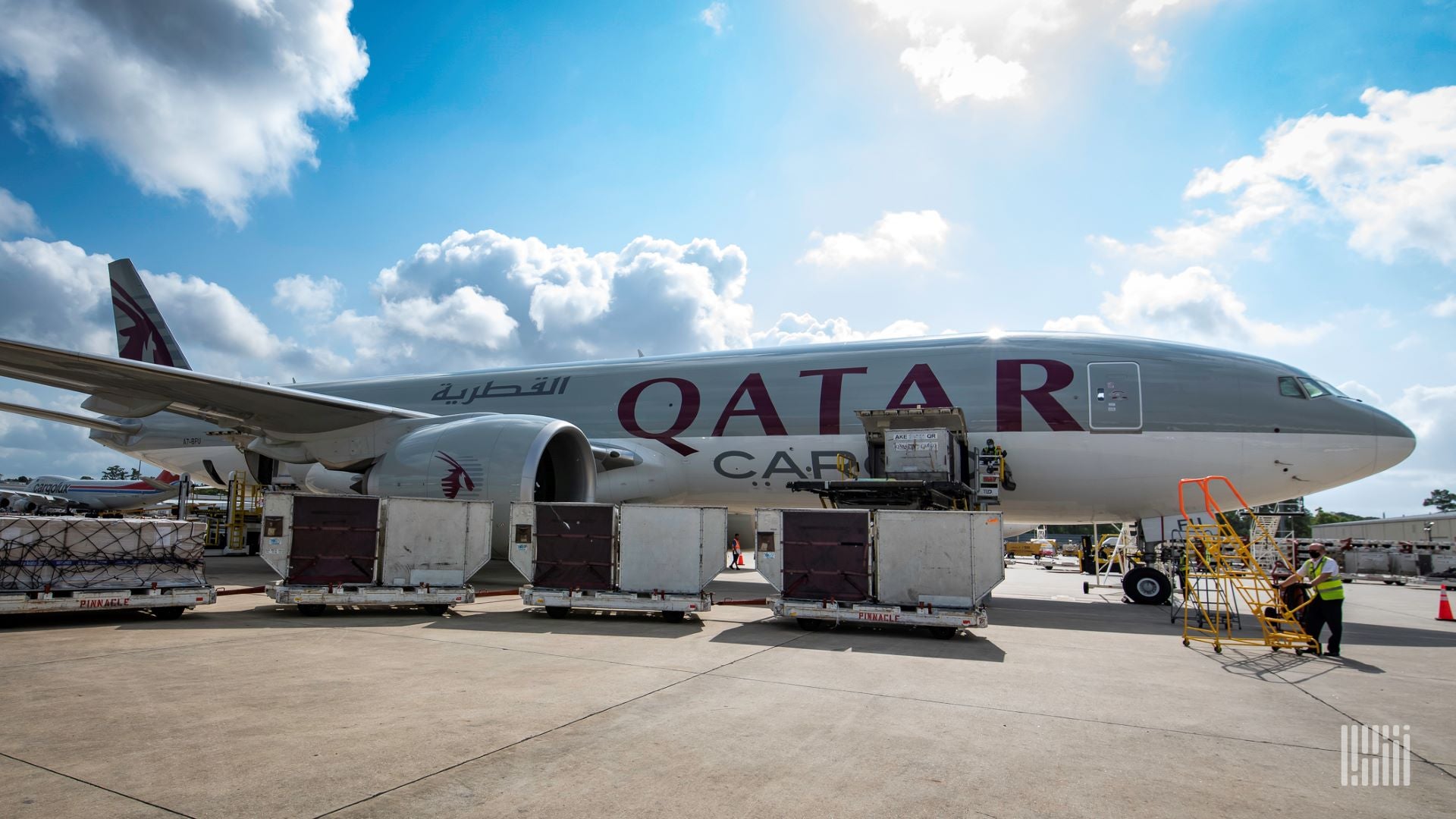 A side view of a Qatar Airways Cargo jet with containers on the tarmac and a sunny day.