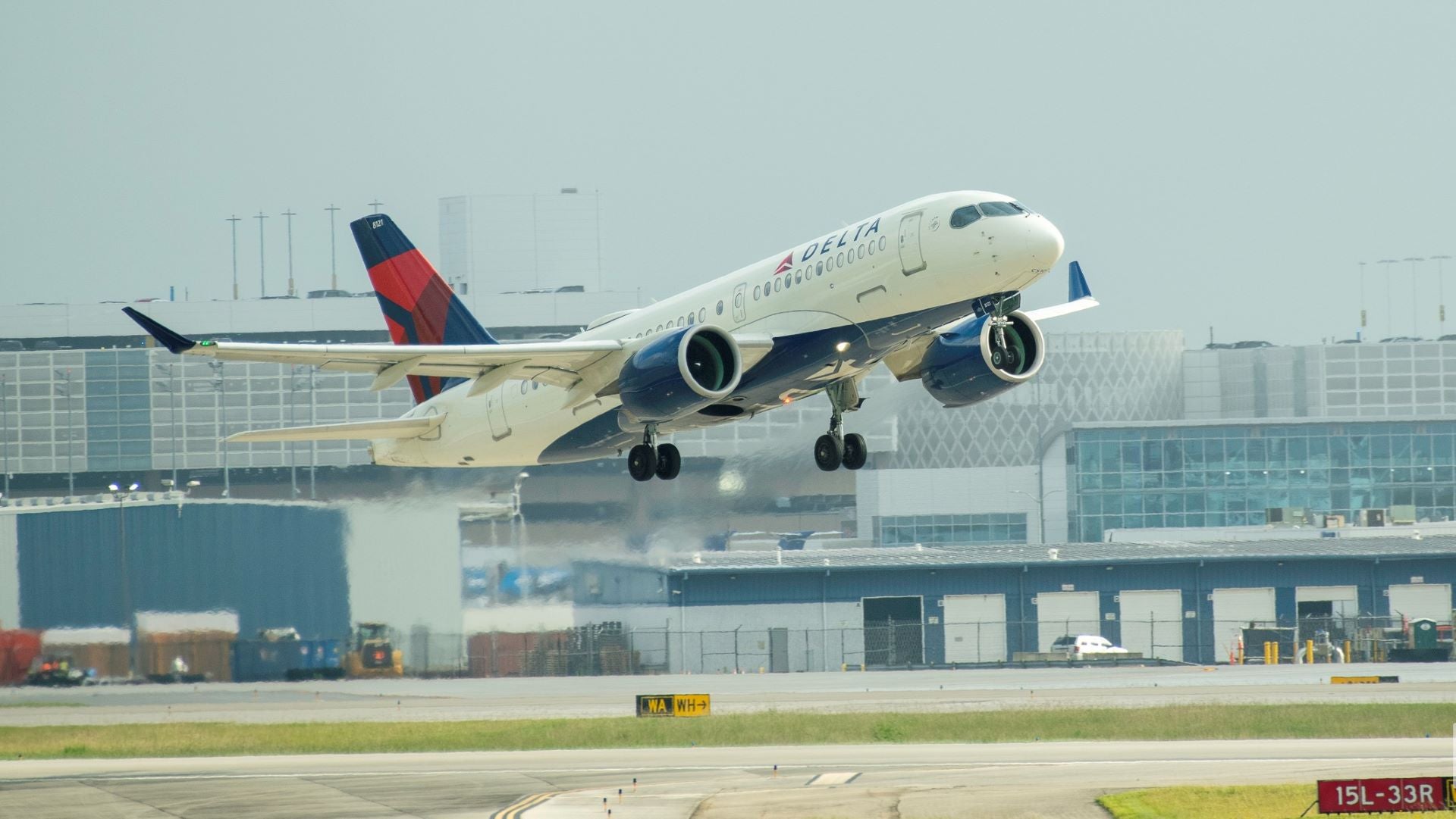 A small Delta jet lifts off runway with airport in background.