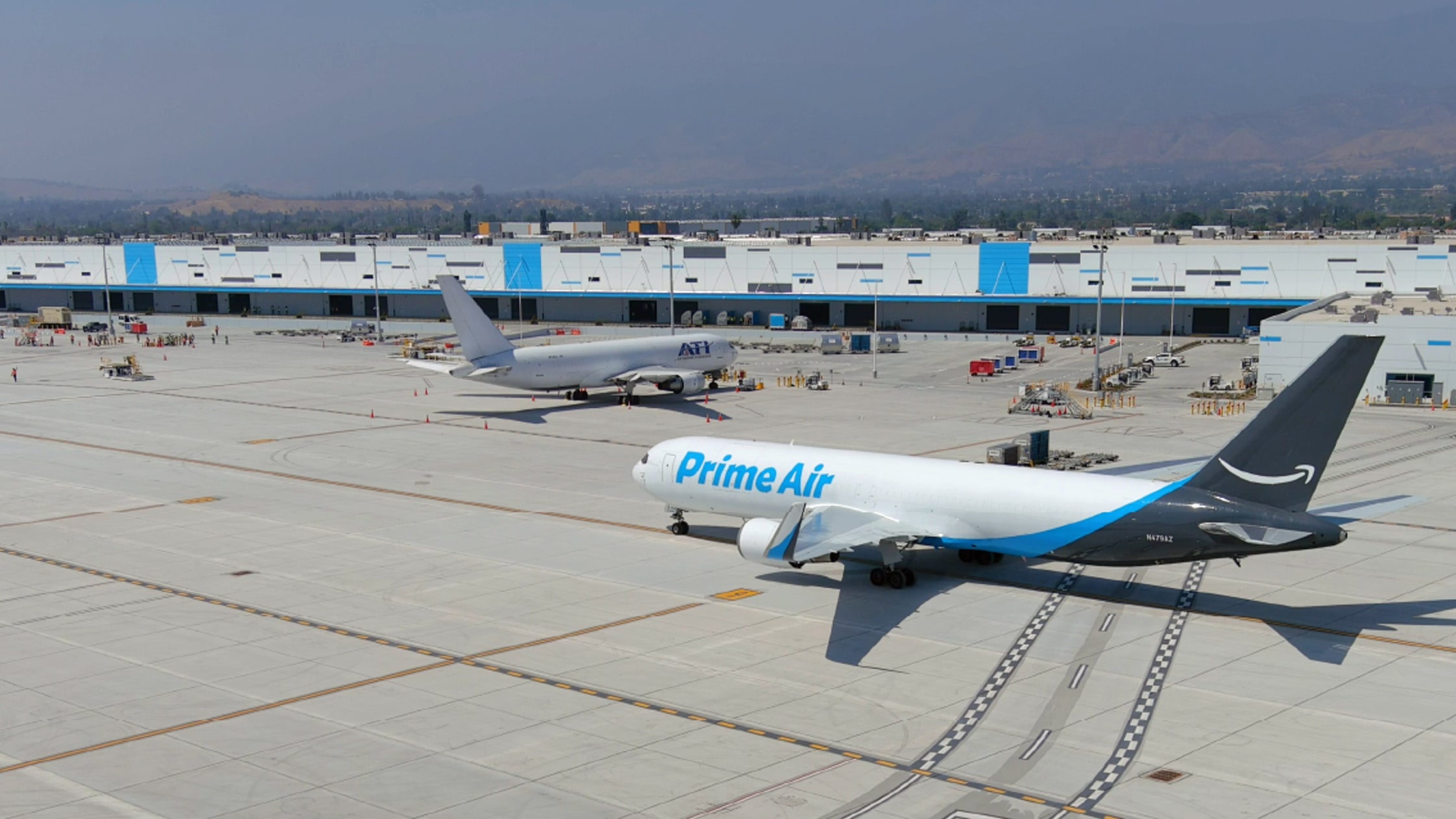 A white plane with pale blue Amazon lettering at a cargo terminal.