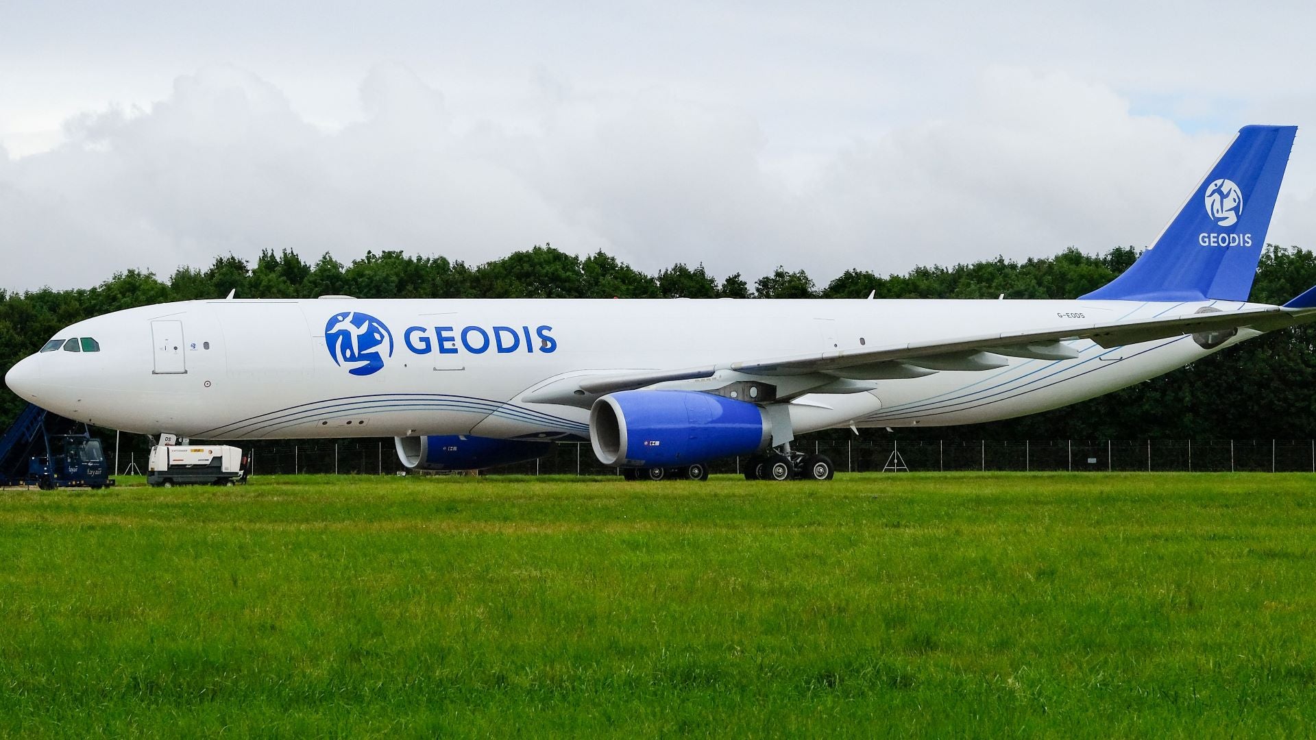 A large white plane with blue GEODIS logo on the side. Grass in the forefront.