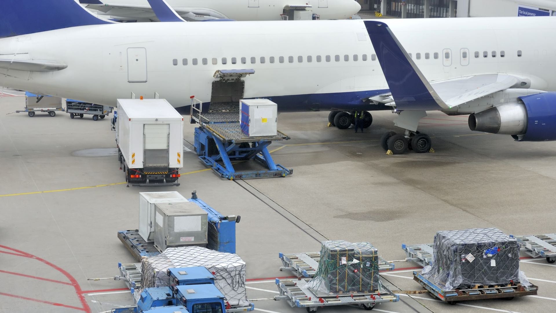 A close up a plane at the gate with cargo containers on the tarmac. View is looking down from the gate.