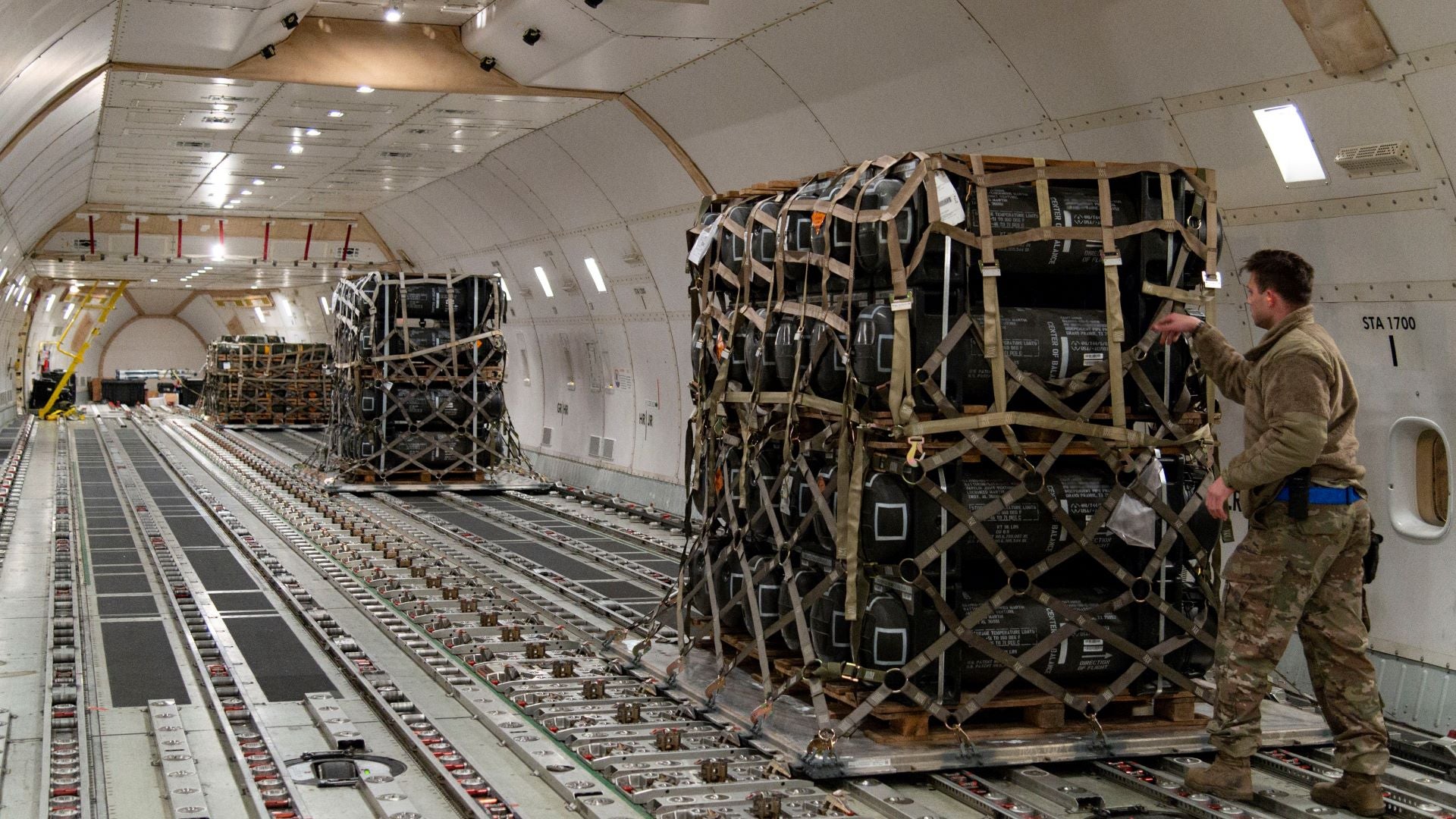 An Air Force service member loads a pallet in the hull of a big cargo airliner.