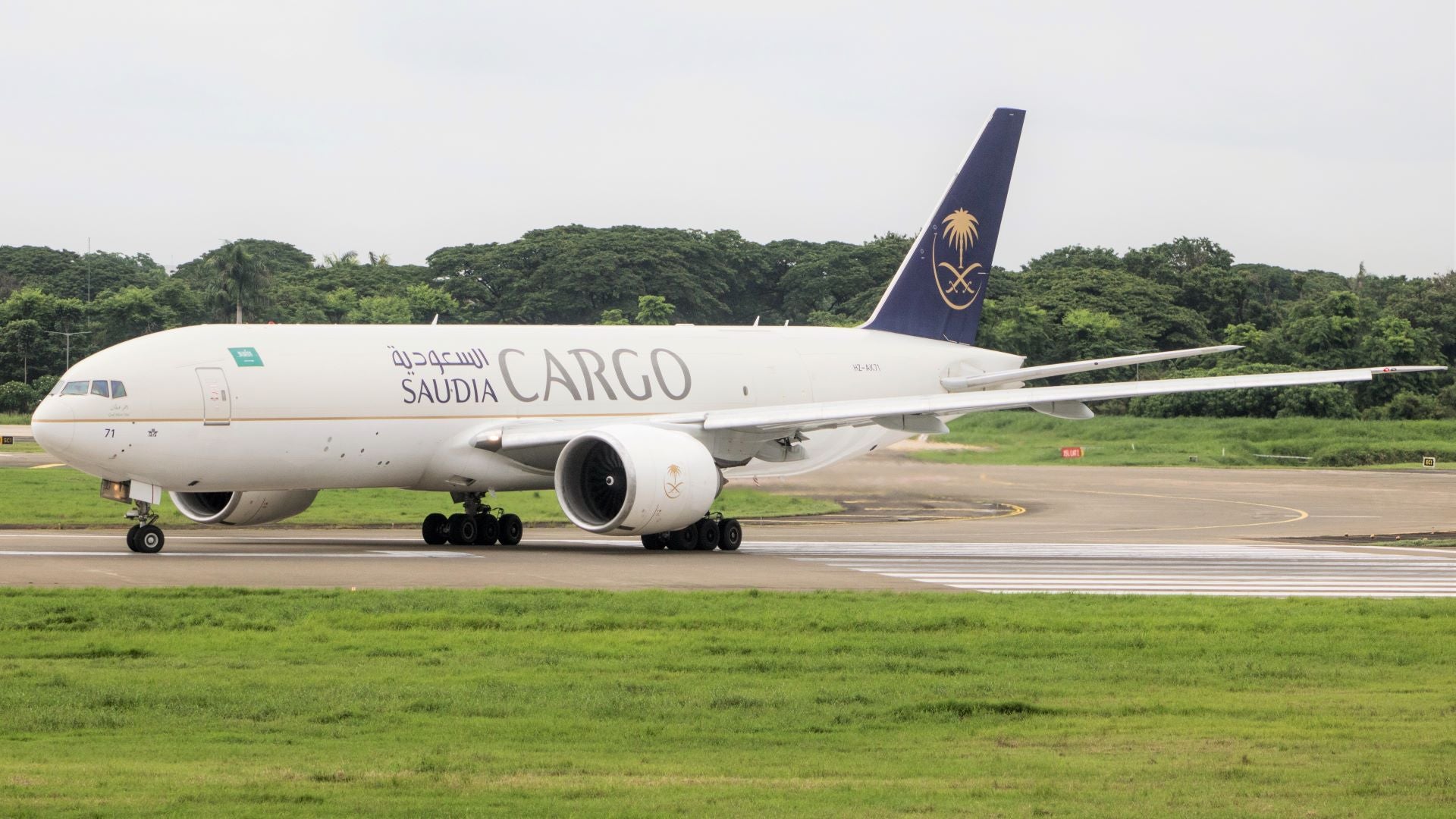 A large Saudia Cargo jet on the runway. White plane with green tail and Arabic lettering.