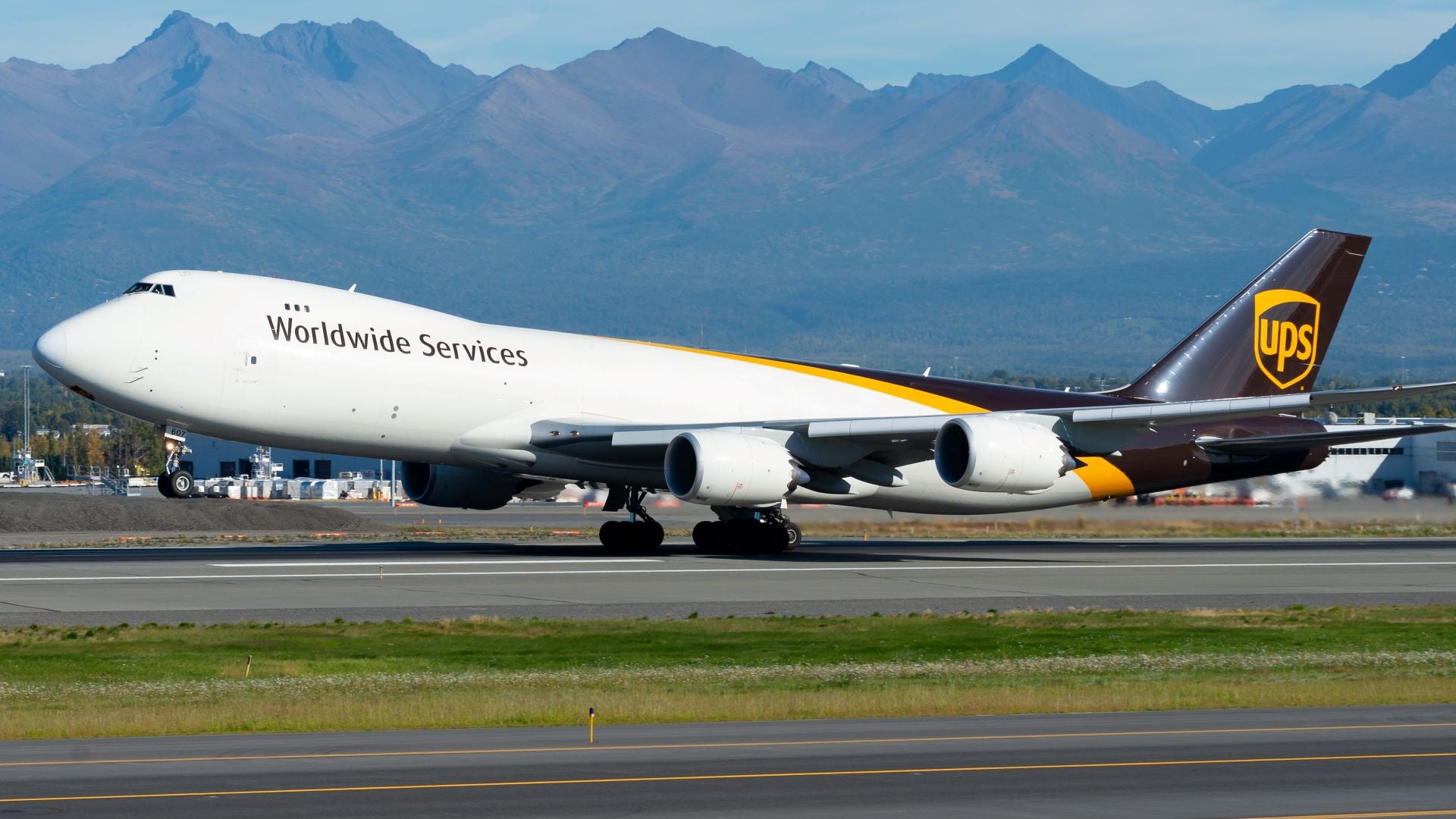 A UPS jumbo jet takes off with mountains in the background.