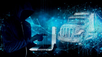 An illustration of a hacker holding a laptop with a tractor trailer to the right.