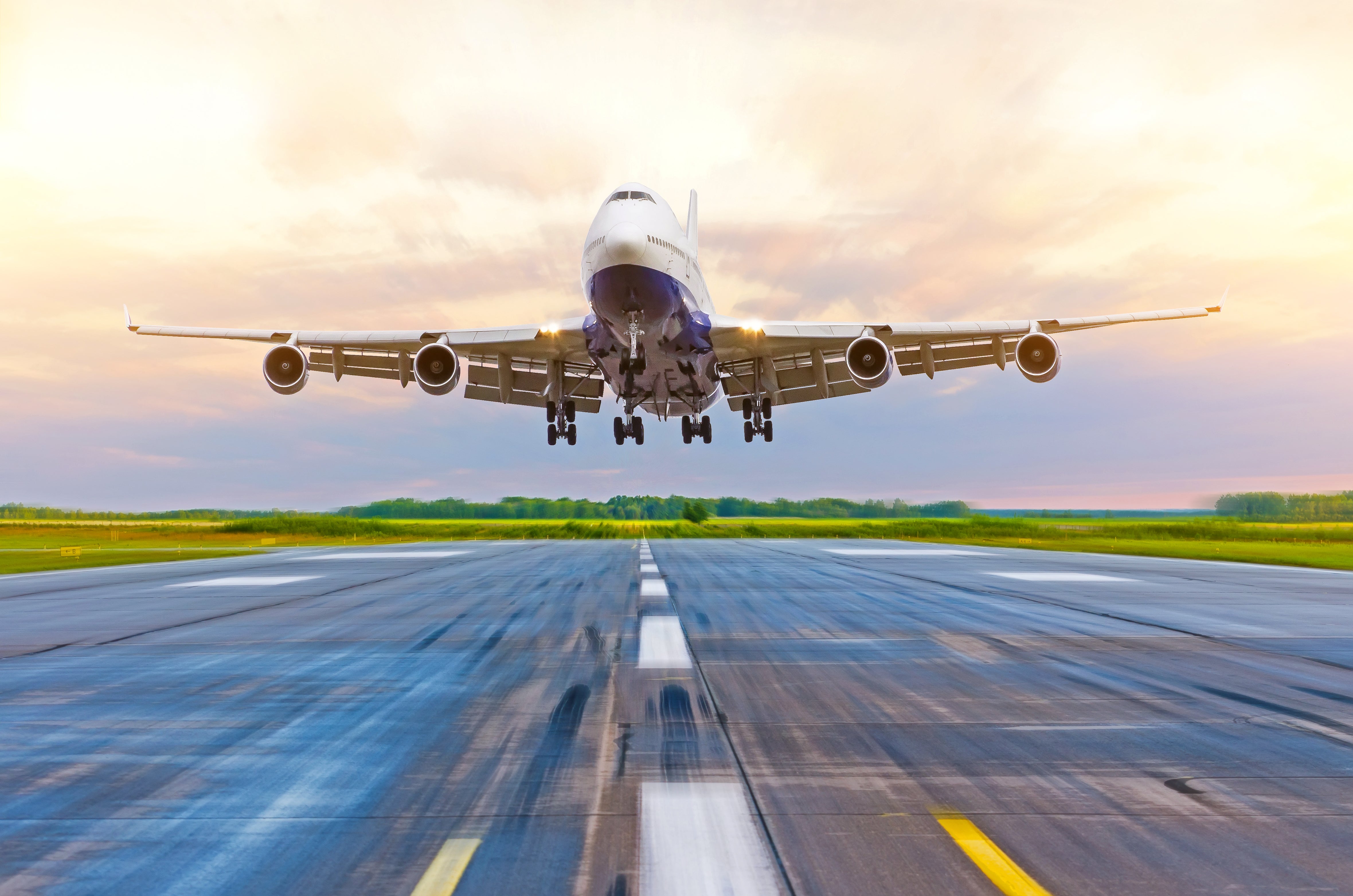 A large jet about to touch down on runway, coming straight at camera with golden sky in background.