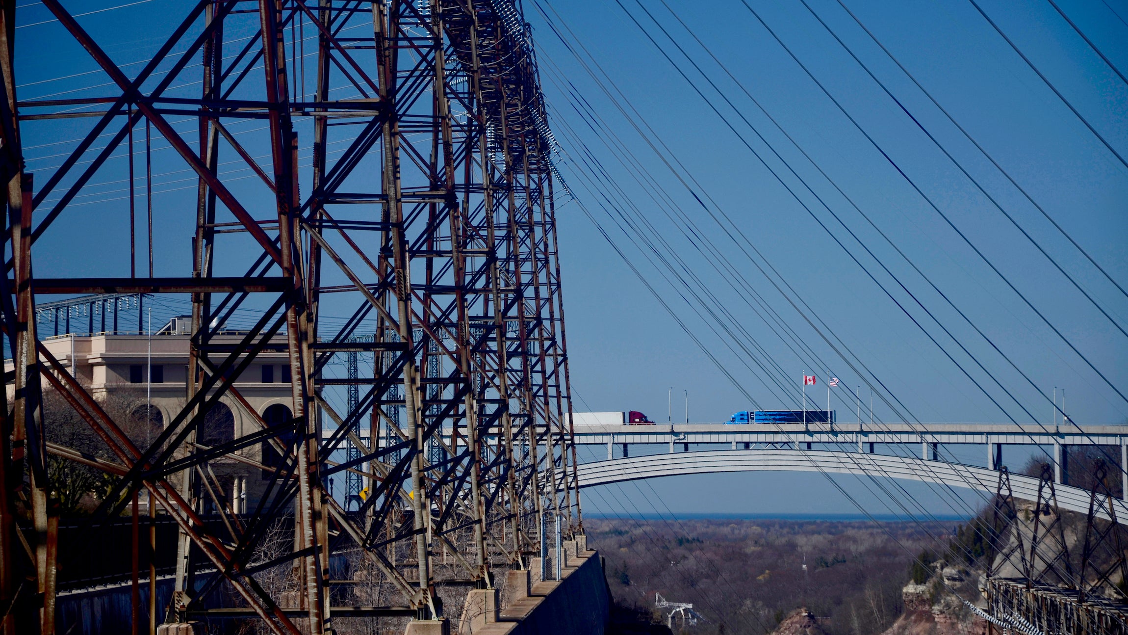 Trucks moving freight across the Canada-US border. With the Sir Adam Beck Power Generating Station in the foreground, and, Lake Ontario on the horizon.