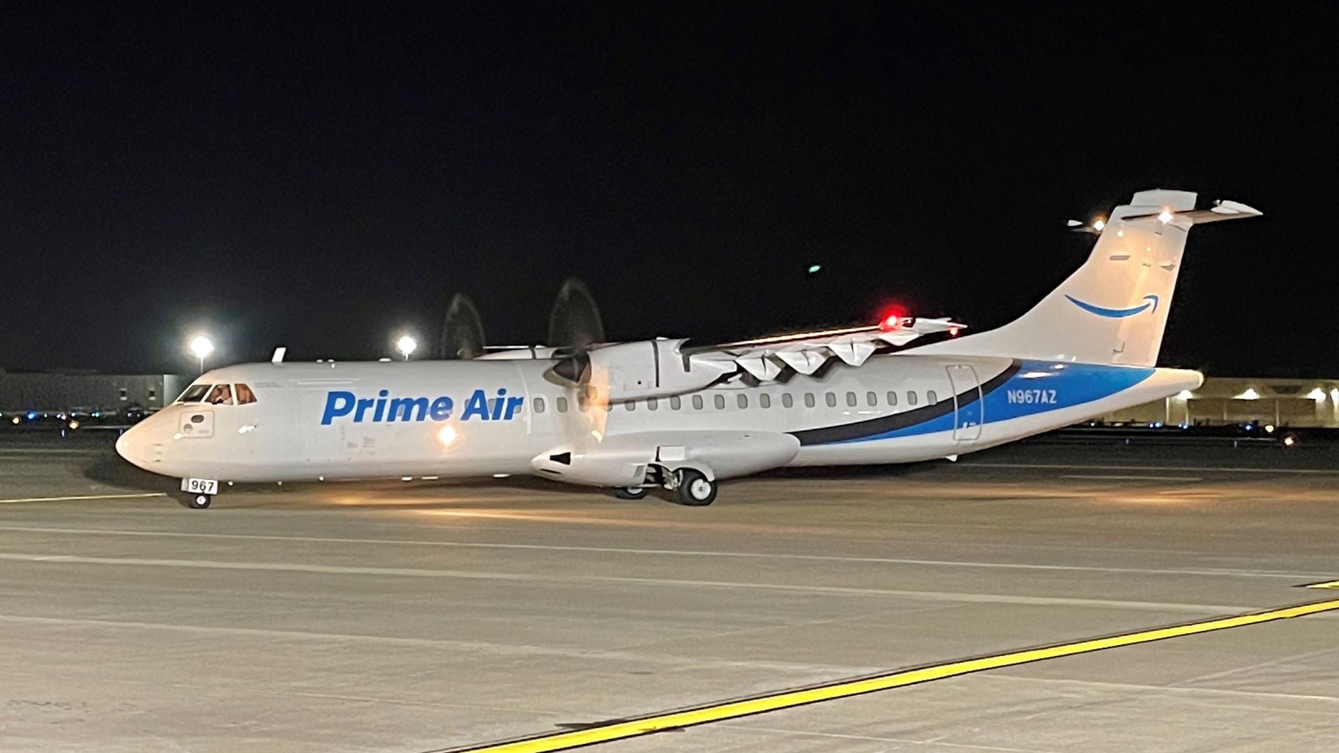 A propeller plane with Amazon Air brand on hull on the tarmac at night.