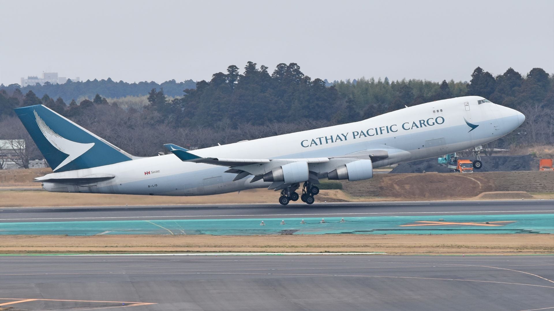 A white jumbo jet with teal tail and Cathay Pacific Cargo lettering lifts off from runway.