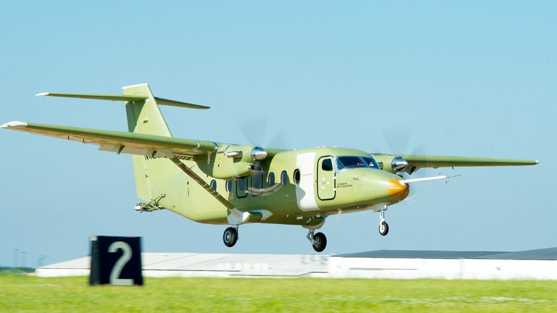 A high-wing turboprop in earth tone color lands on runway.