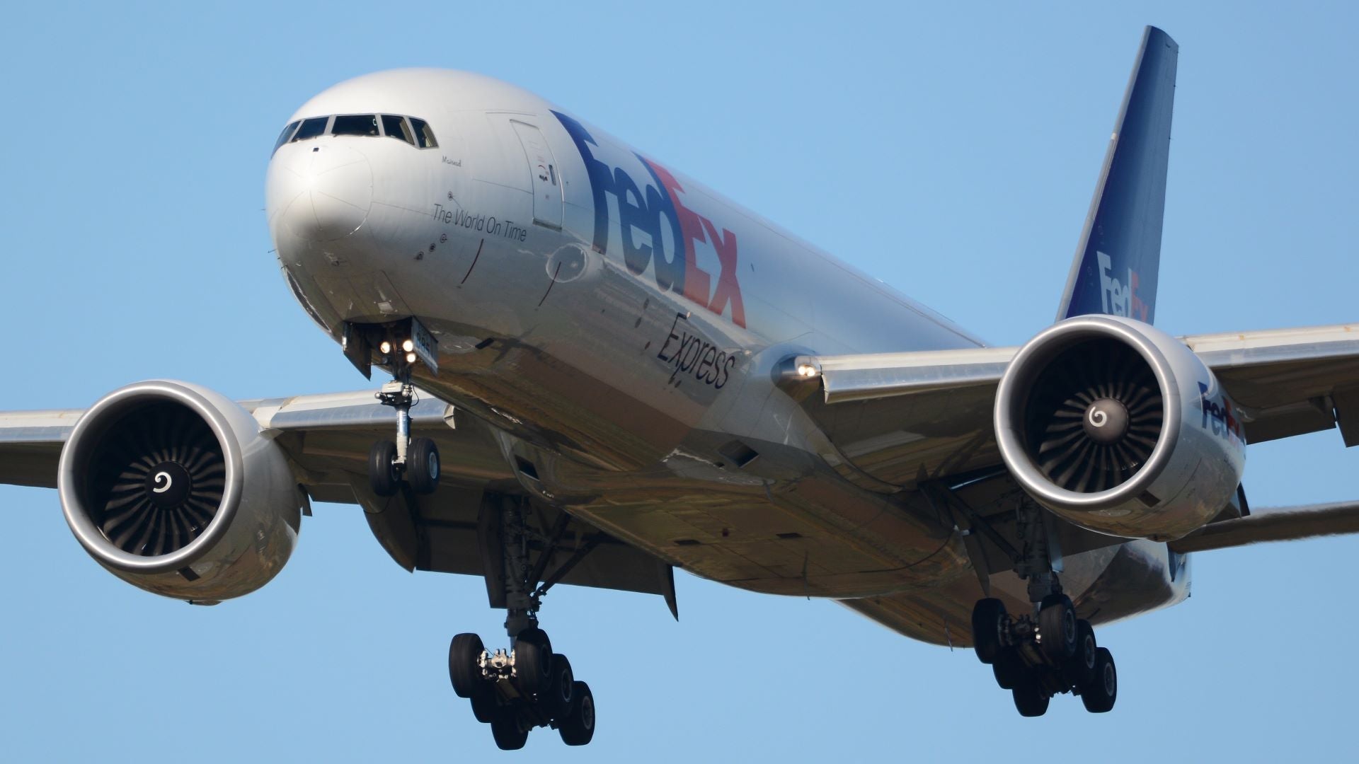 A big FedEx freighter coming in for landing, close up view of front with wheels lowered.