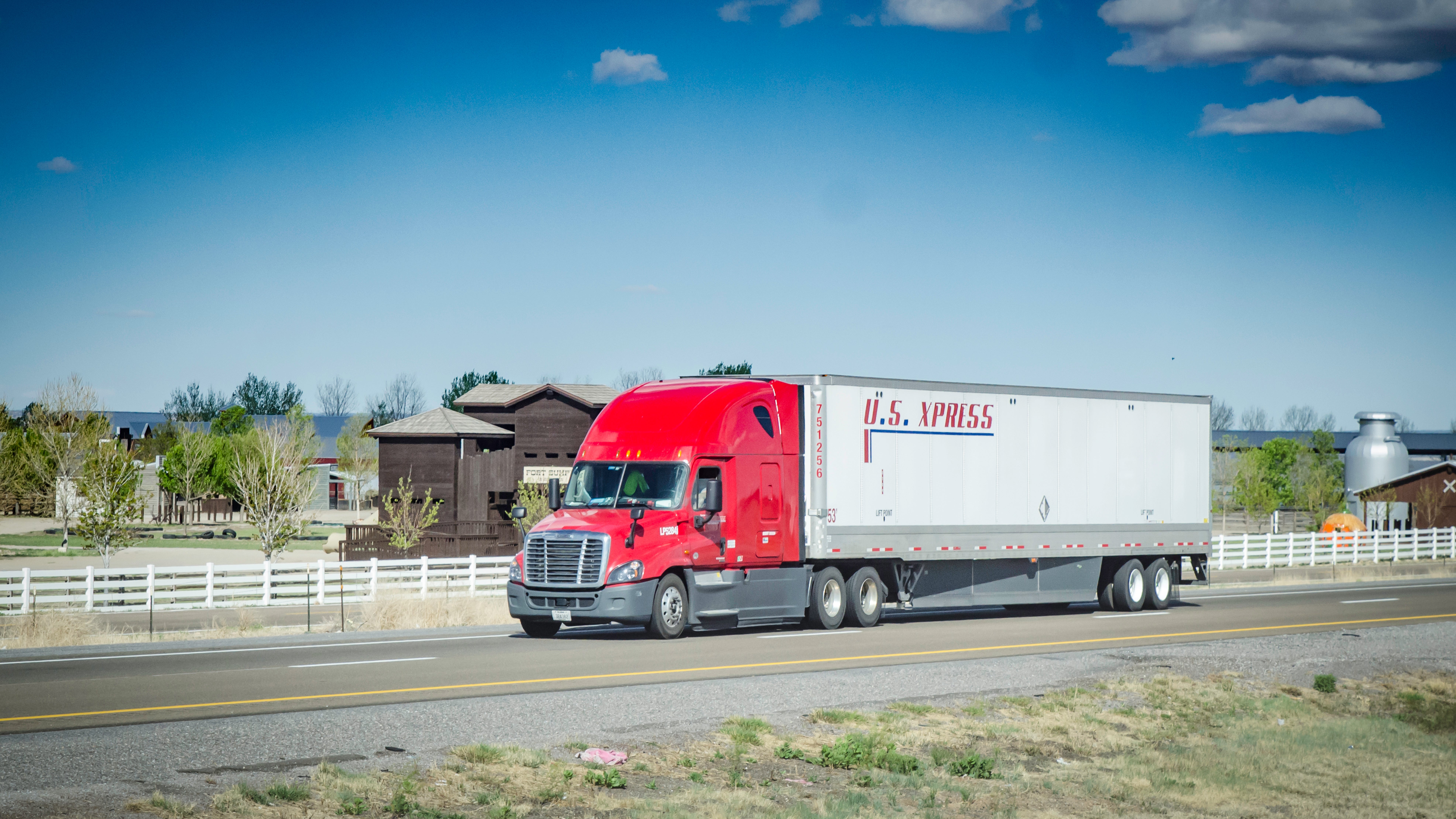 A red and white tractor-trailer of the company US Xpress travels on a road