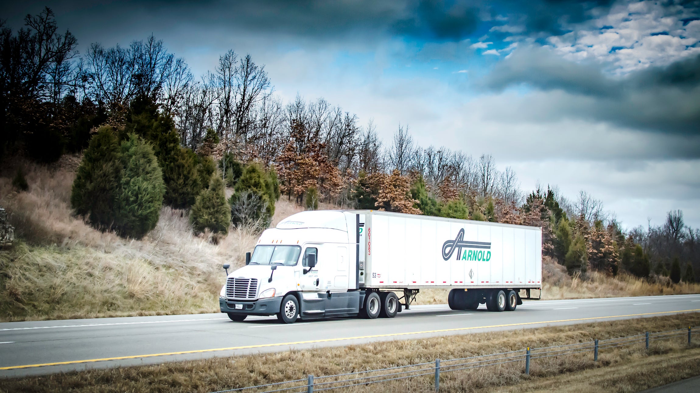 A tractor-trailer with the logo of Texas trucking company Arnold Transporation Services travels on a road seen from the side