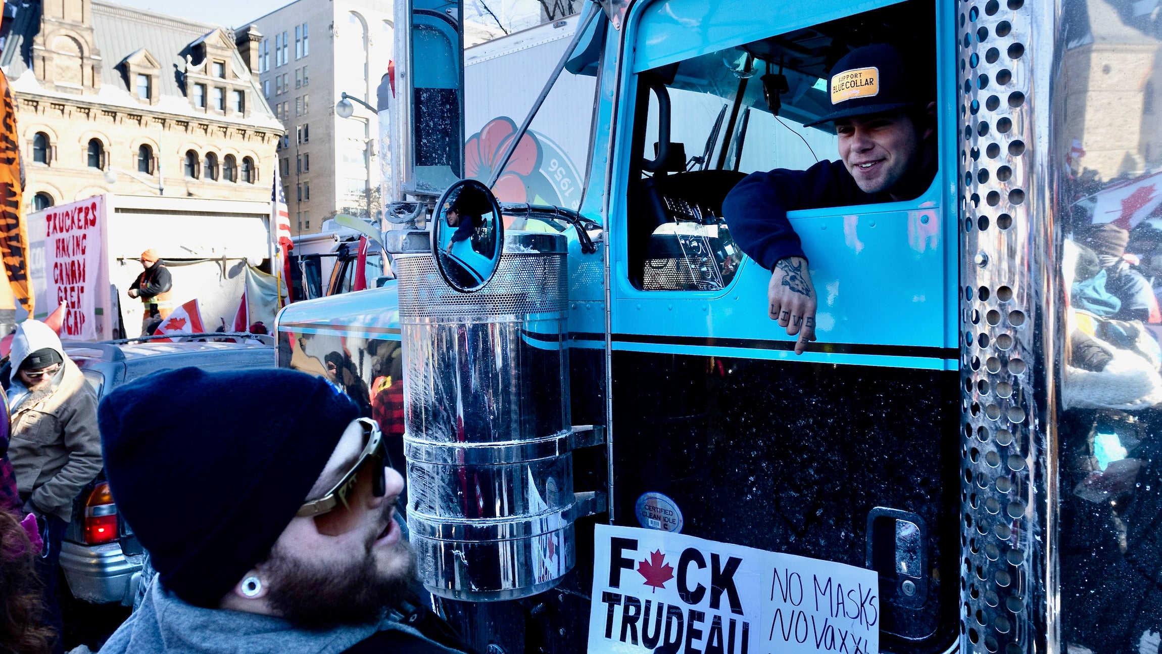 A truck driver wearing a hat talks to a man holding a protest sign at the Freedom Rally in Ottawa.