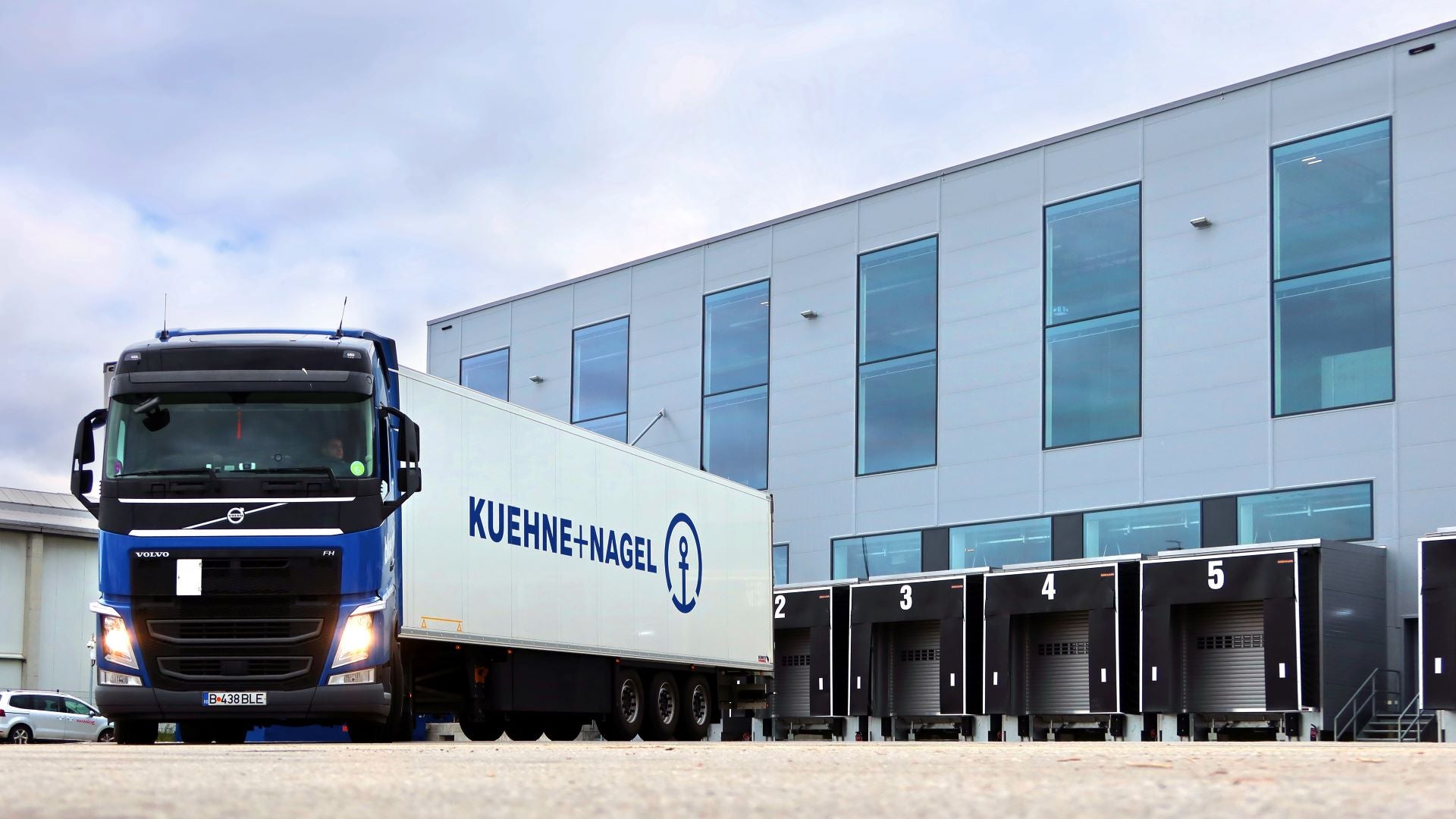 A blue and white Kuehne + Nagel truck in front of loading docks.