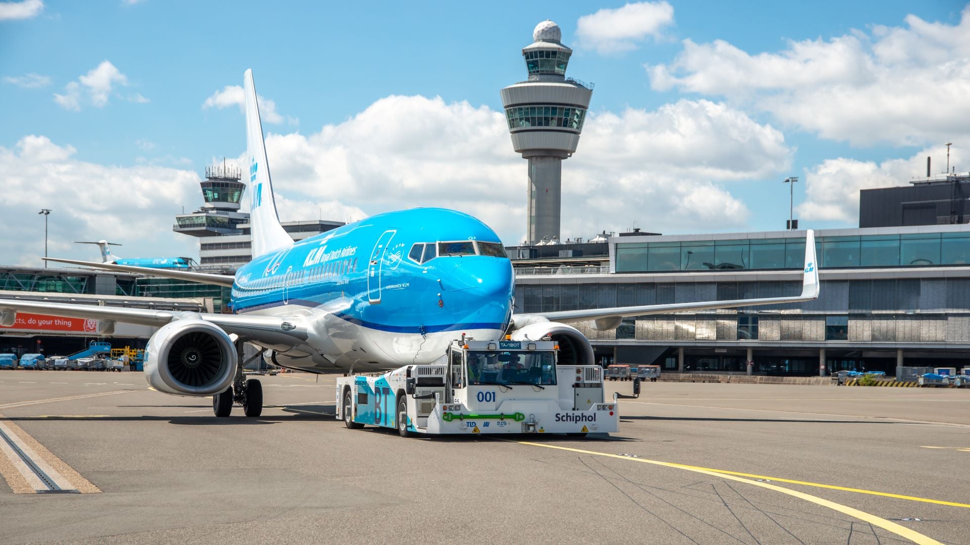 A light blue KLM jet with front wheel attached to a tow vehicle.