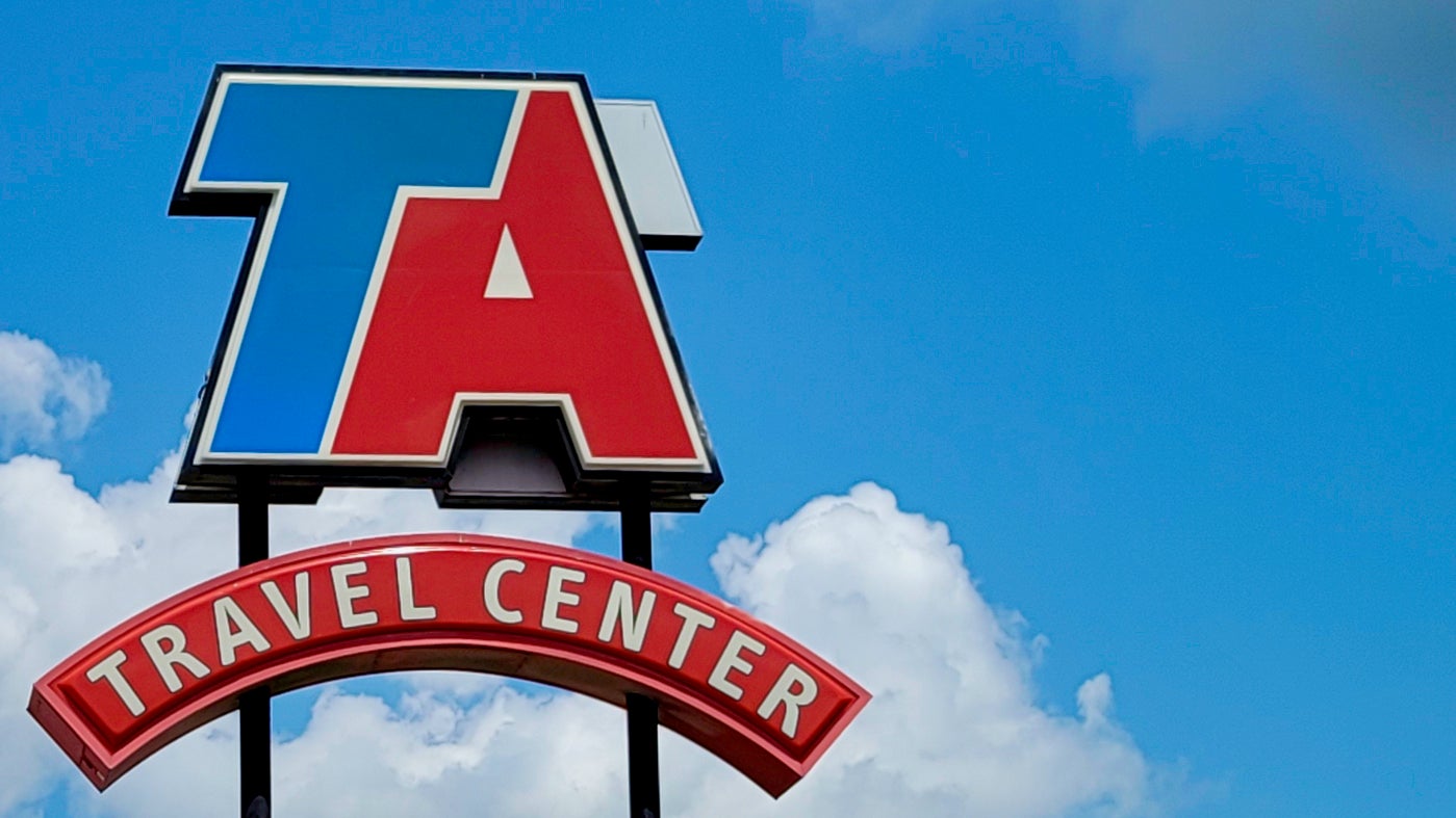 A sign with.the logo of TravelCenters of America with a blue sky in the background