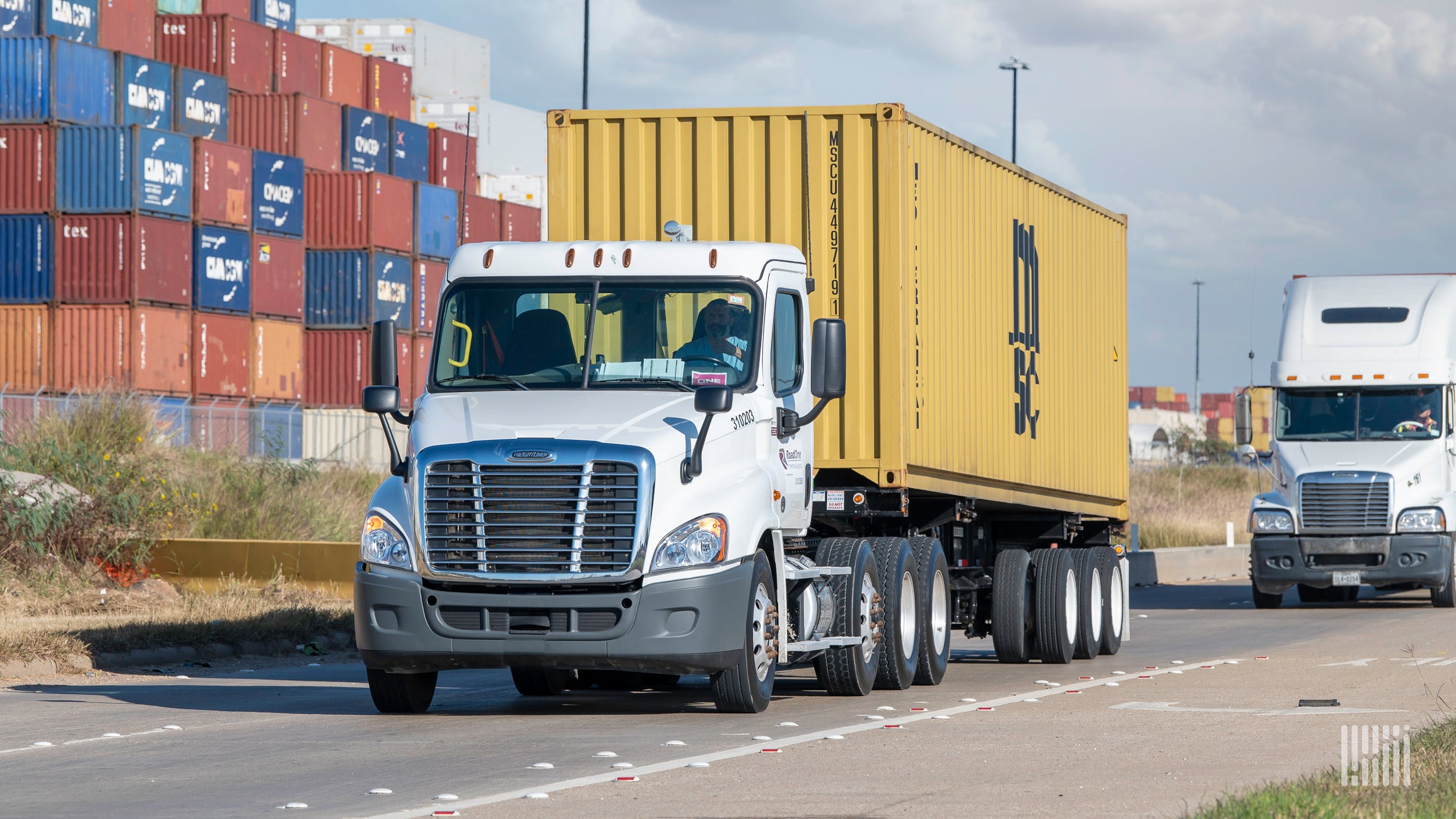 A yellow container on a white truck leaving the Port of Houston