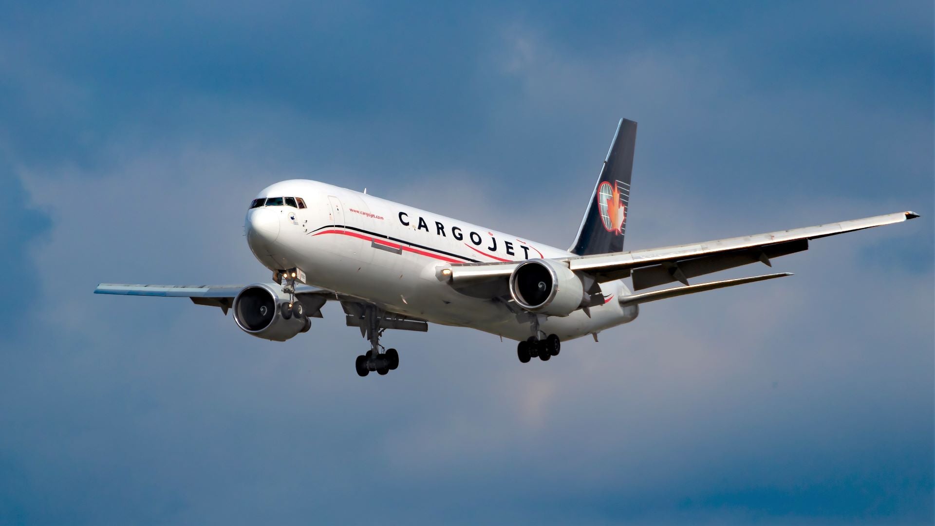 A Cargojet 767, white body with dark blue tail, comes in for landing with wheels down against cloudy sky.