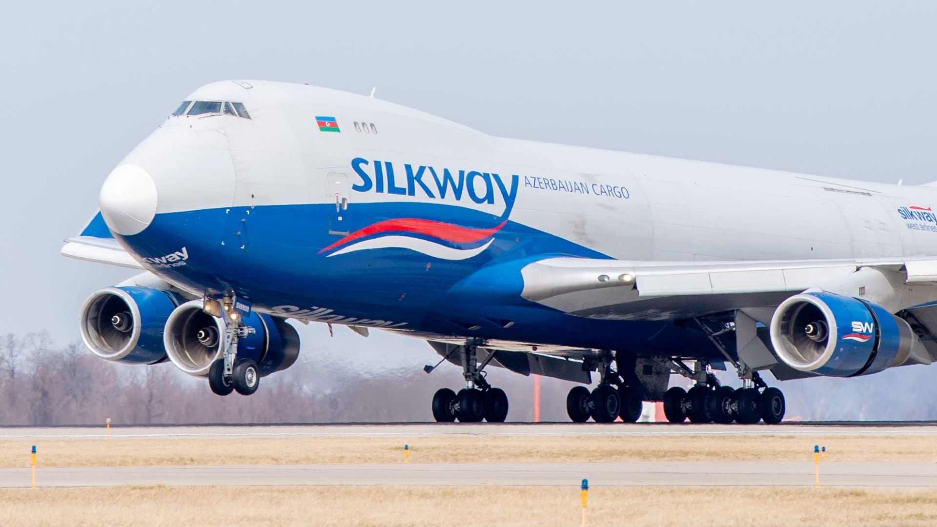 A white-and-blue Silk Way jumbo jet touches down on runway. Silk Way is carrying freight from Asia to Cincinnati airport each week.