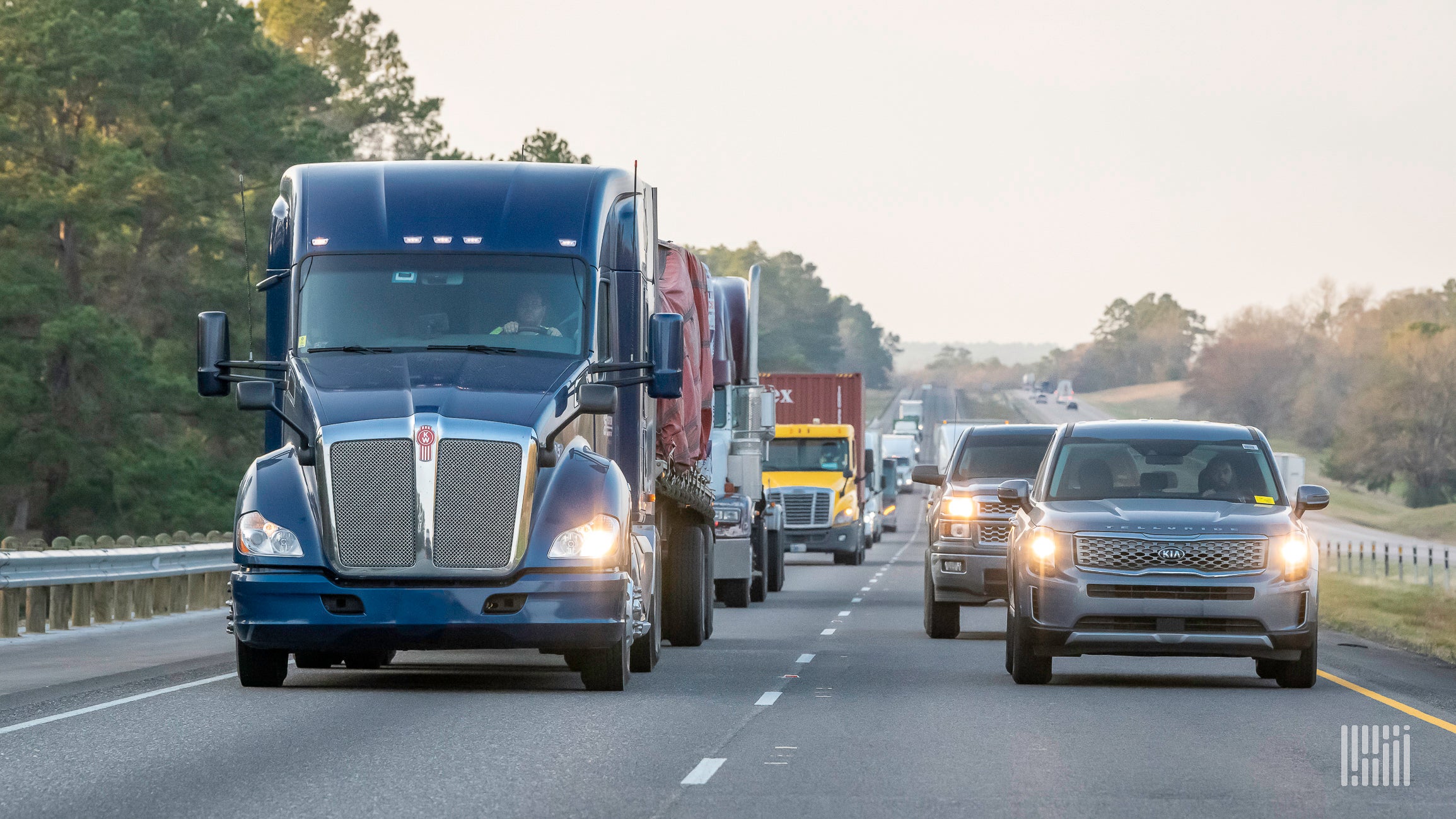 A line of trucks traveling at the same speed as passenger vehicles in the left lane