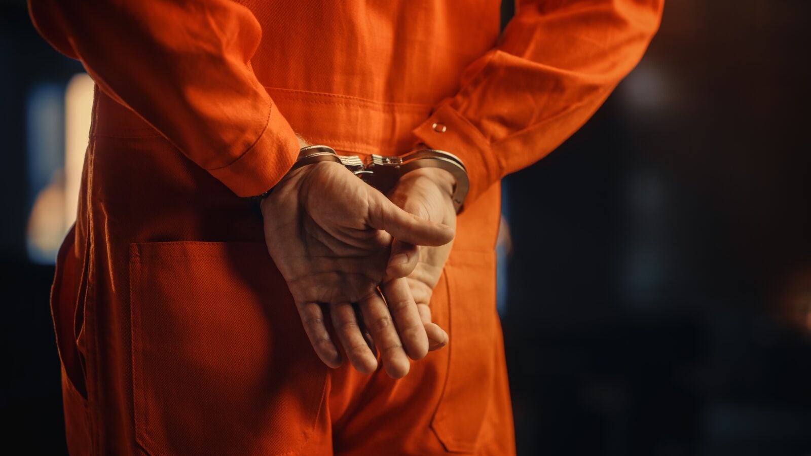 A person in an orange jail jumpsuit with their hands cuffed illustrating a person getting sentanced