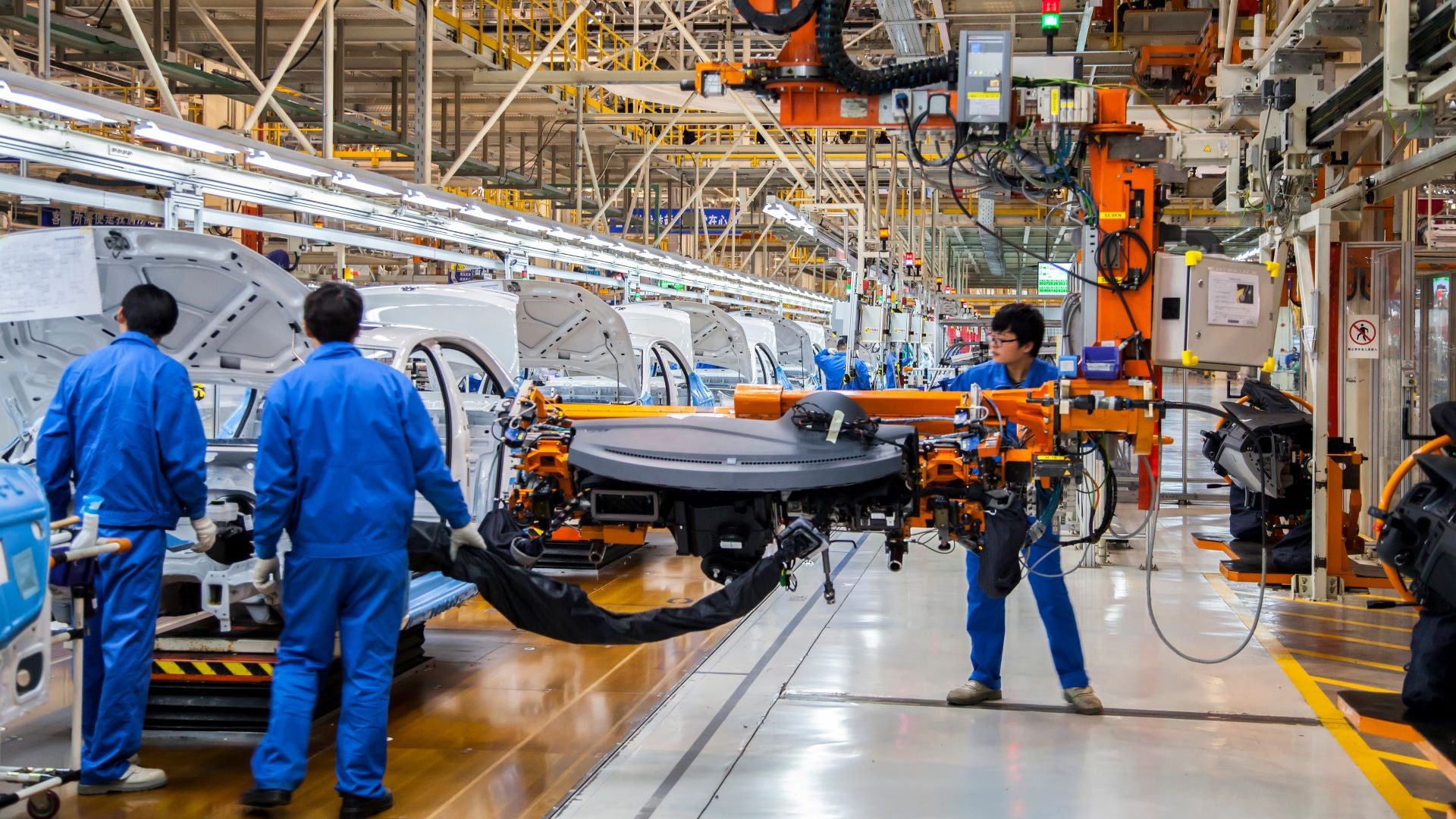 An automotive assembly line in China with workers in blue suits handling machinery.