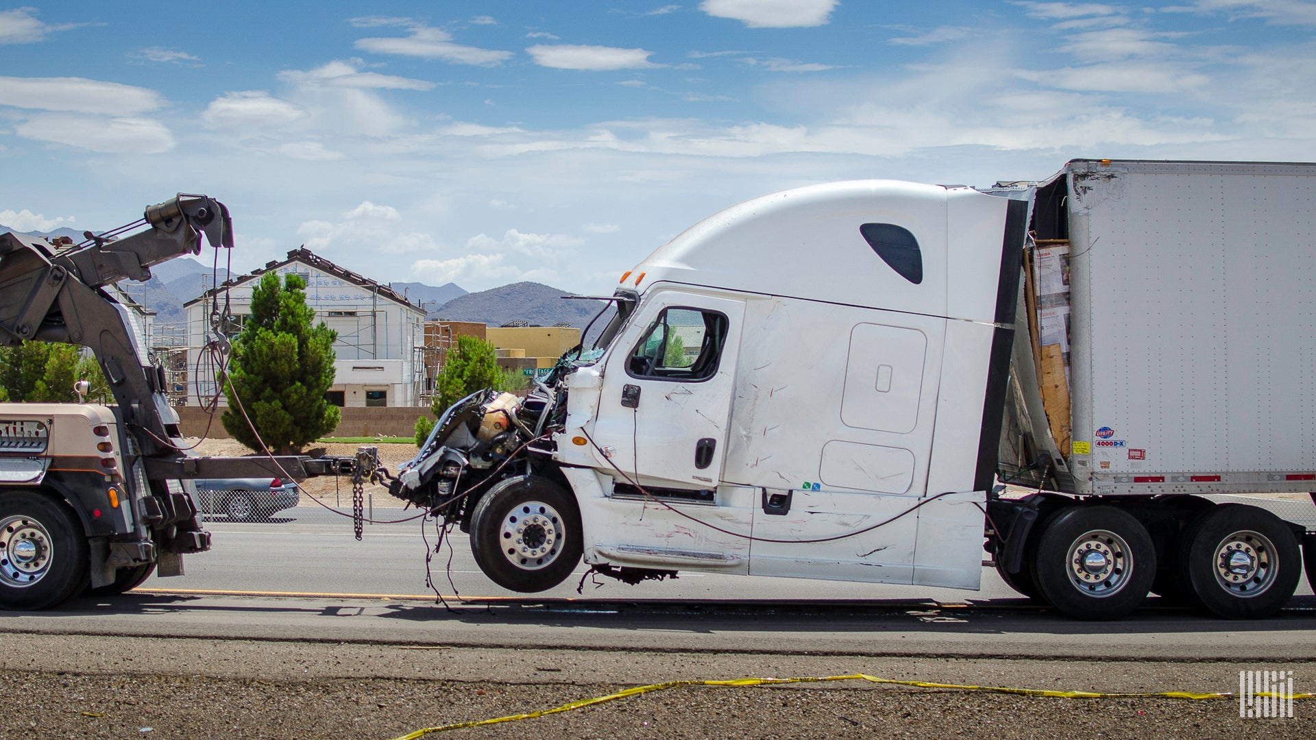 A commercial truck that has been damaged in an accident in attached to a tow truck.