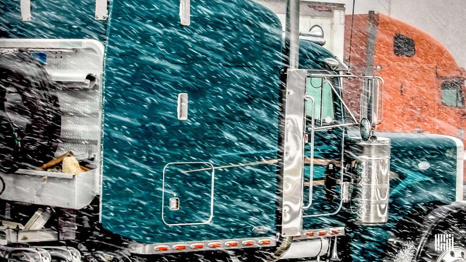 An orange and blue tractor-trailer travels through a blizzard