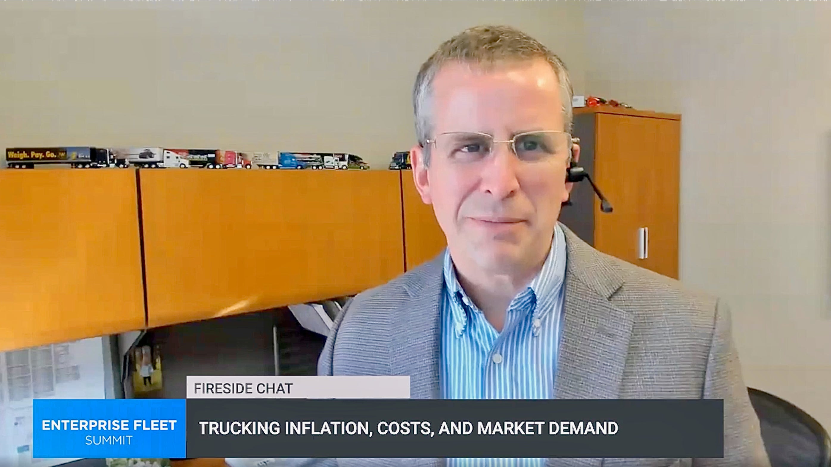 A man in a sport coat standing in front of cabinet that has miniature trucks on top of it.