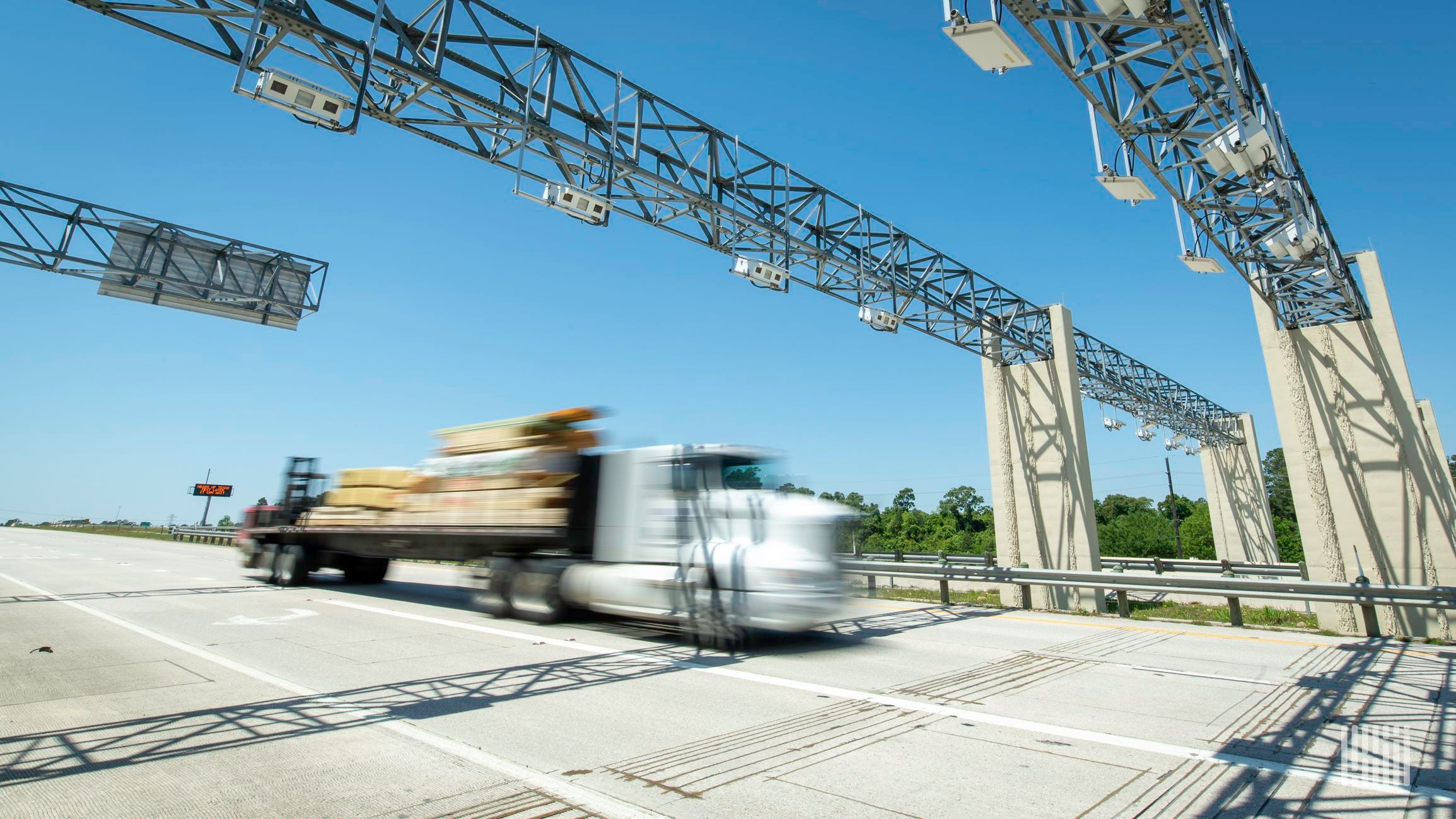 A flatbed truck passes under a bridge