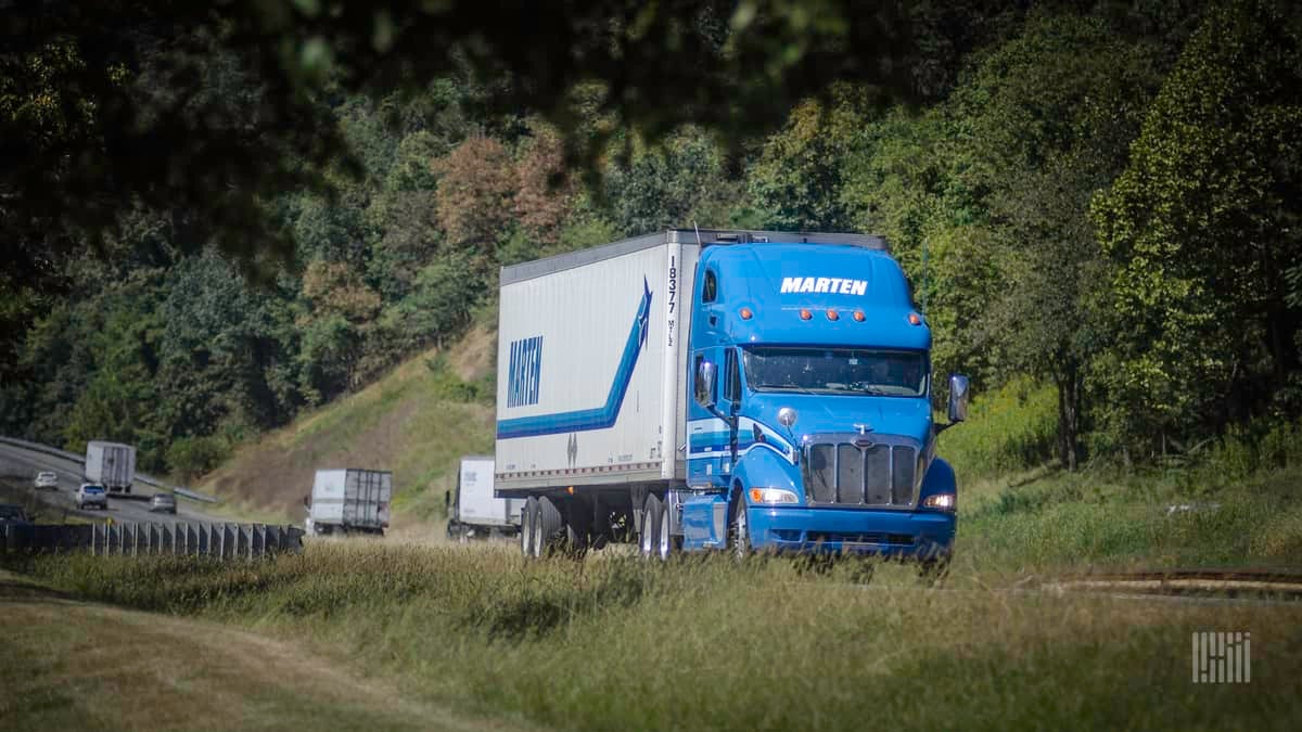 A blue and white commercial truck with the logo of Marten Transport traveling on a road