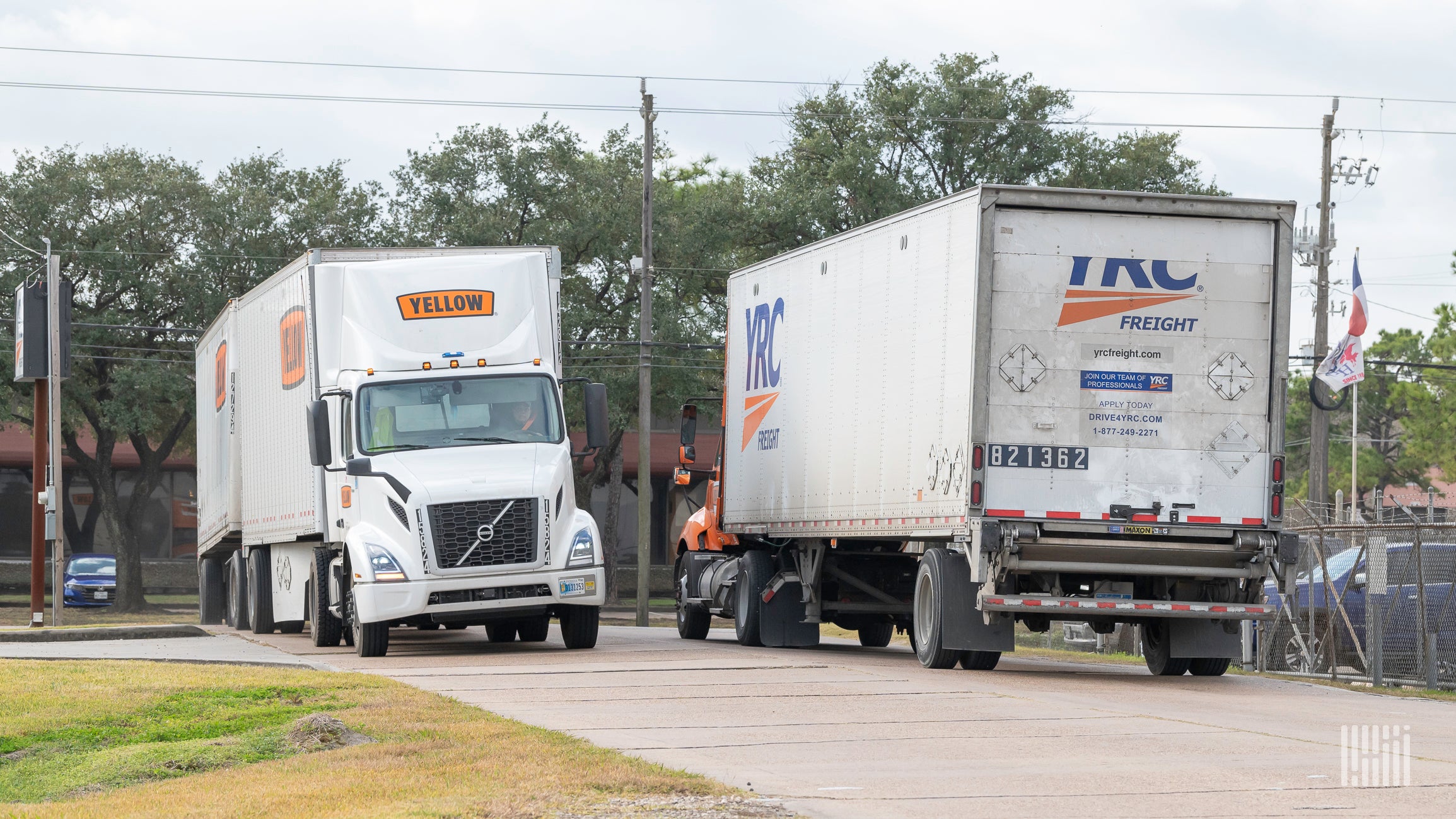 A white Yellow Corp. tractor with two Yellow trailers passing a YRC Freight truck near a terminal