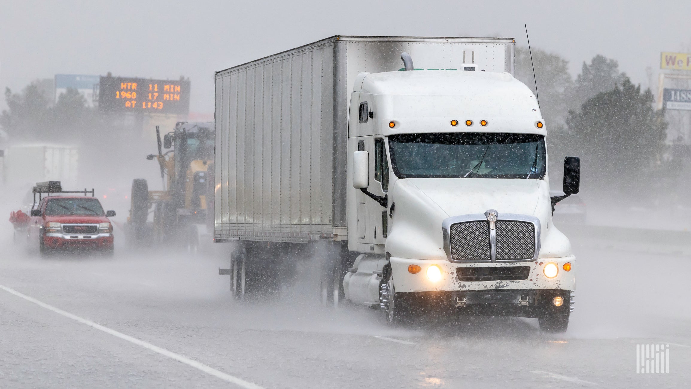 A White tractor, silver trailer on highway in rain storm