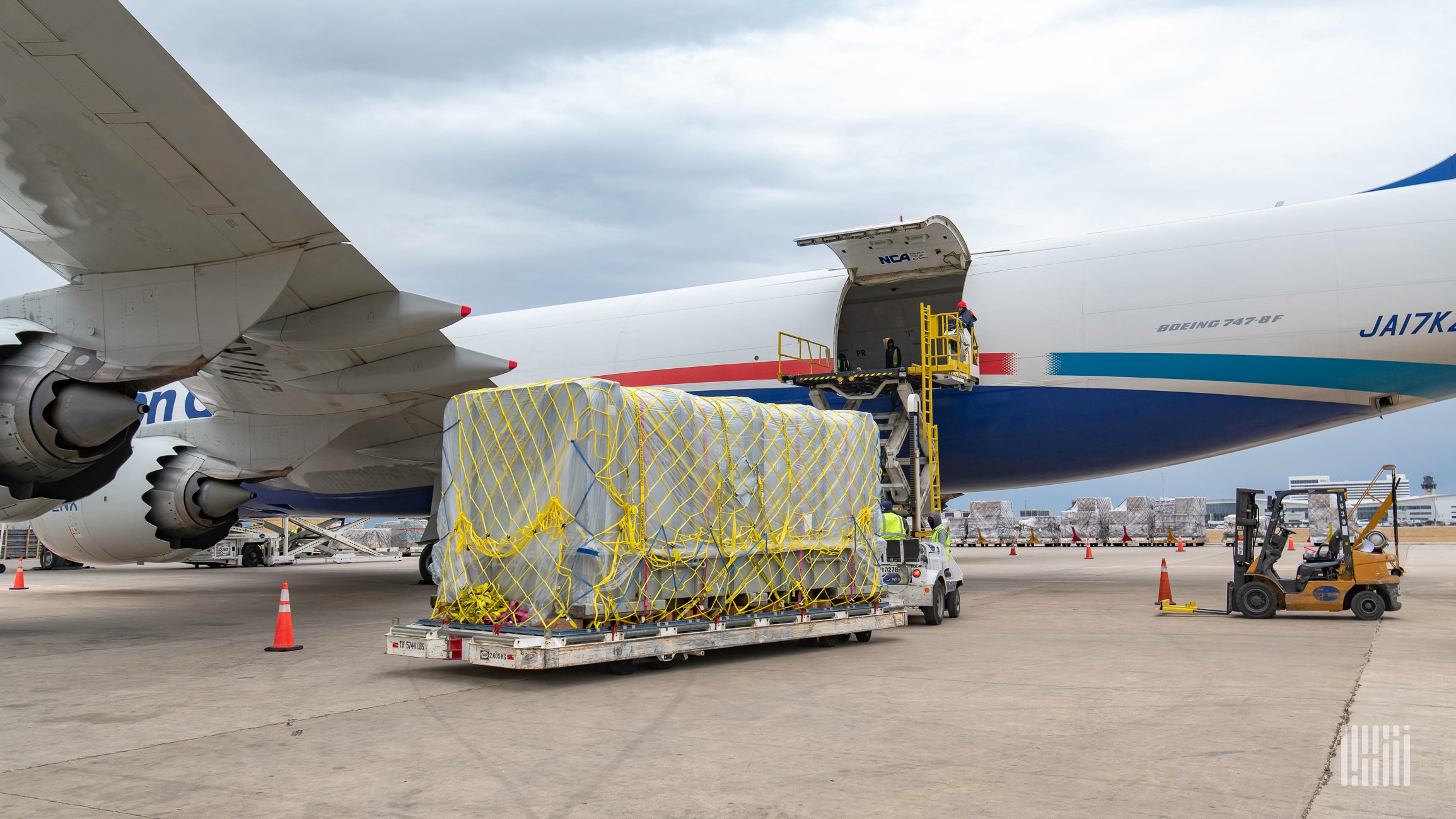 A large cargo pallet on the tarmac waiting to be loaded in the open door of a large jet.