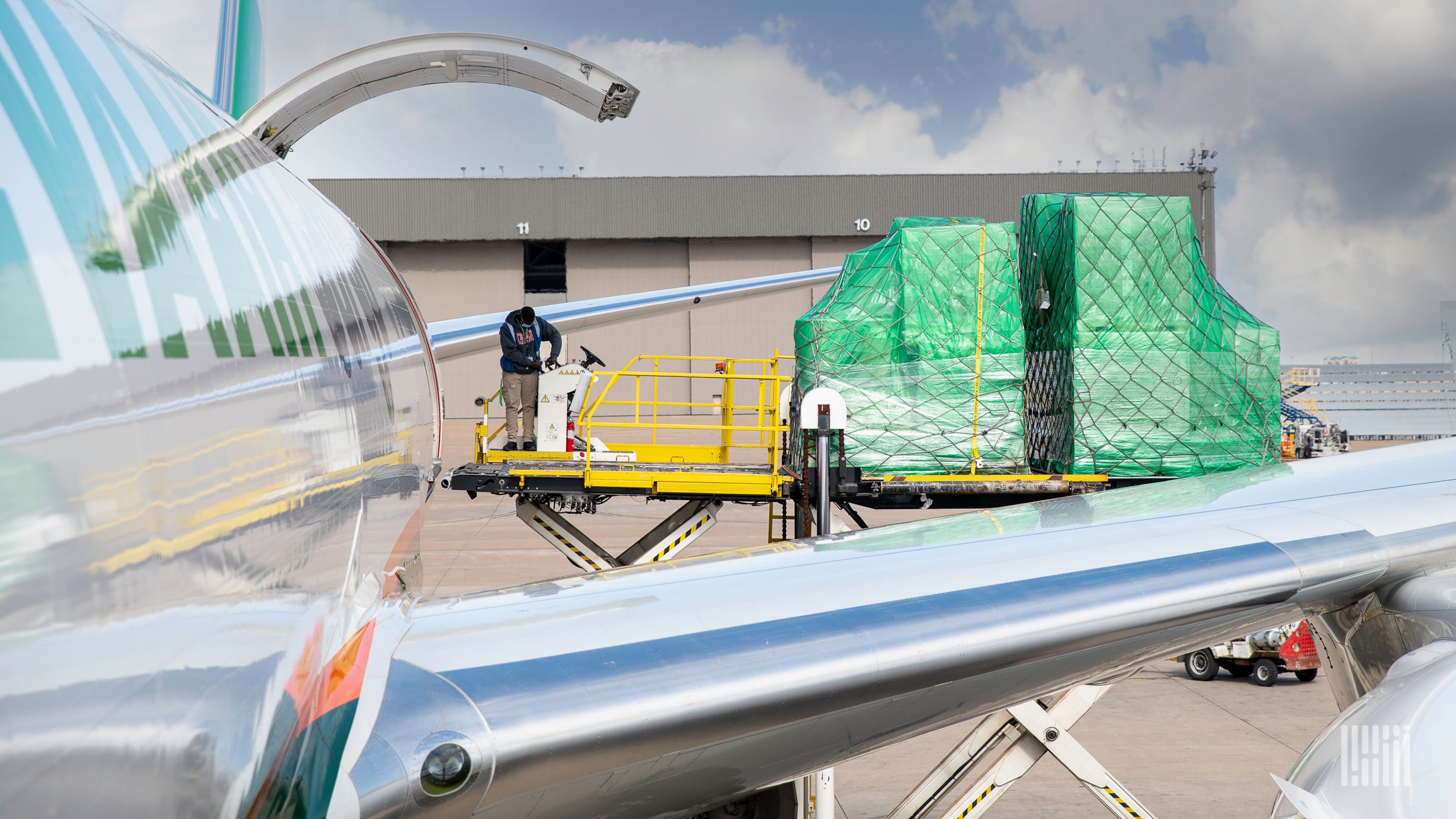 A pallet of cargo being loaded from a hoist into the upper deck of a plane as viewed from the side of plane over the wing.