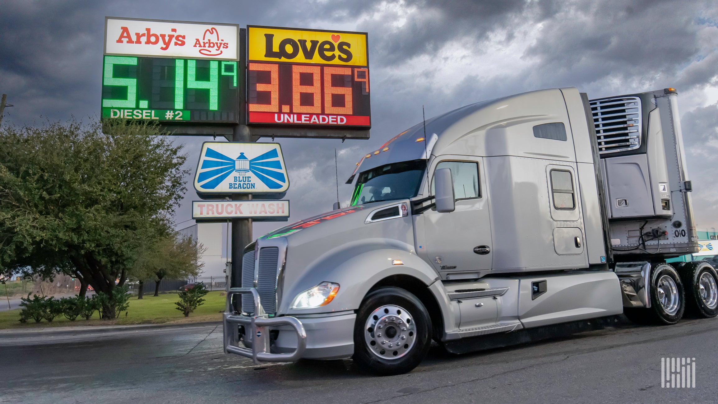 A white semi truck next to a sign showing diesel and regular gas prices