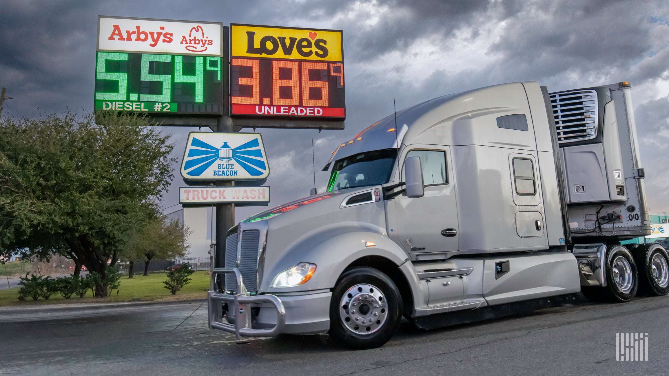 A silver tractor-trailer travels in front of a Love's and Arby's sign with high diesel prices.