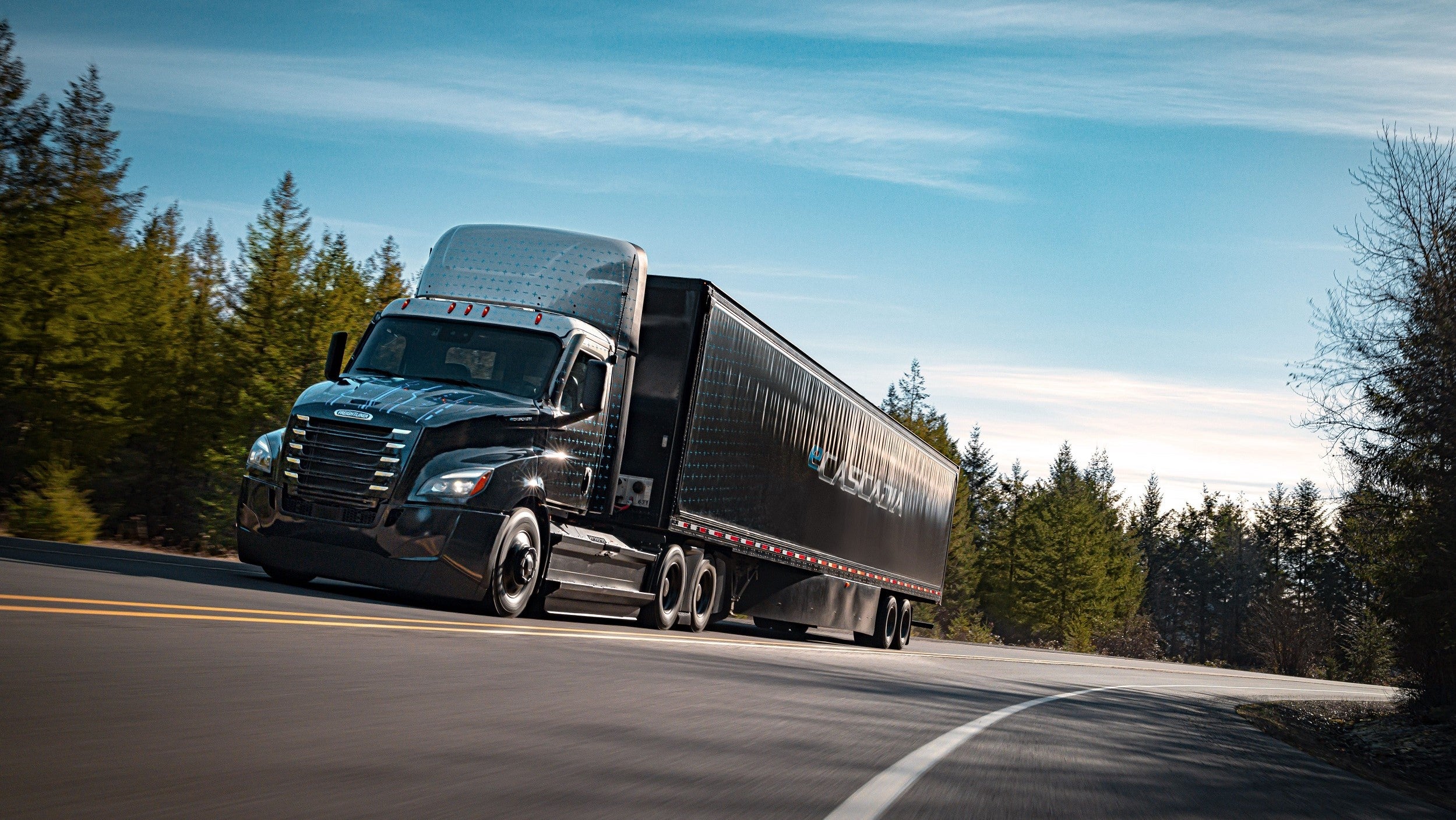 Freightliner eCascaida on sloped highway backed by pine trees